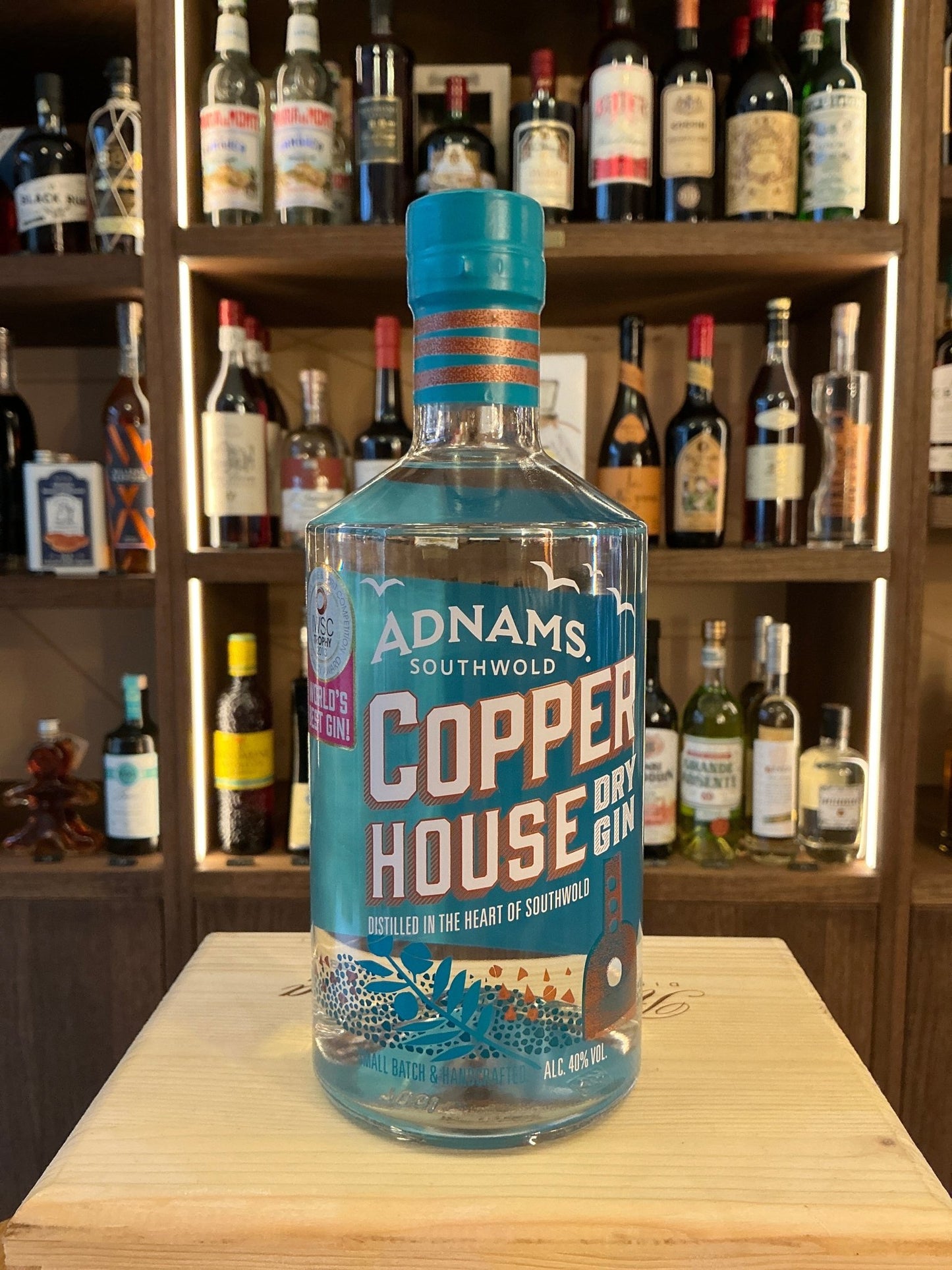 Adnams Copper House Dry Gin bottle with blue and copper label, artisan small batch botanical gin on wooden surface.
