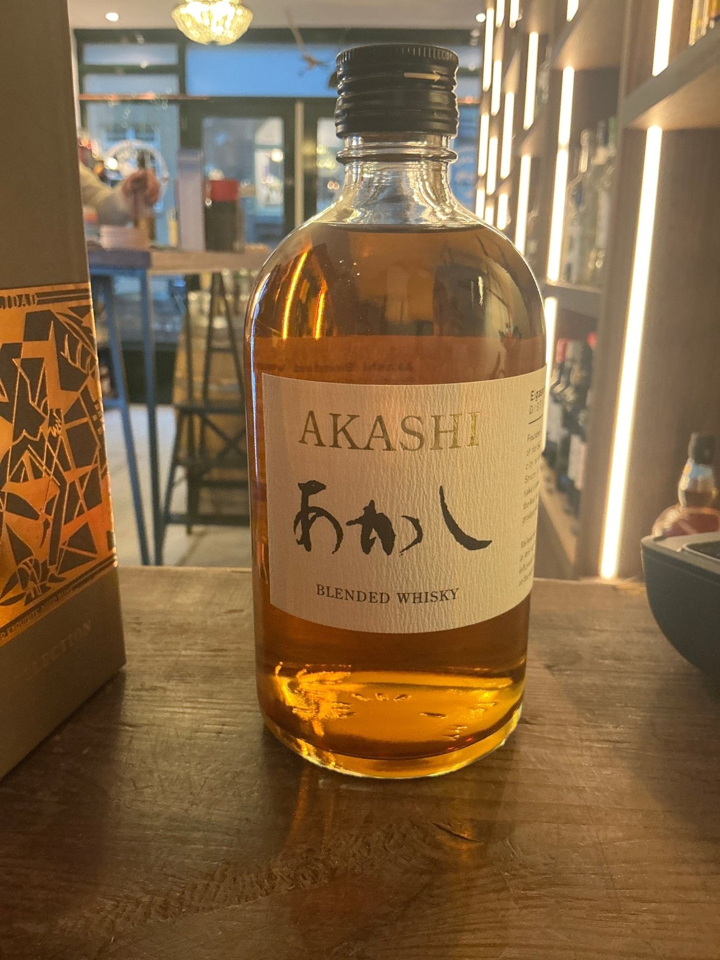 Clear glass bottle of Akashi Blended Whisky with amber liquid, black cap, and Japanese script label, artisan small batch.