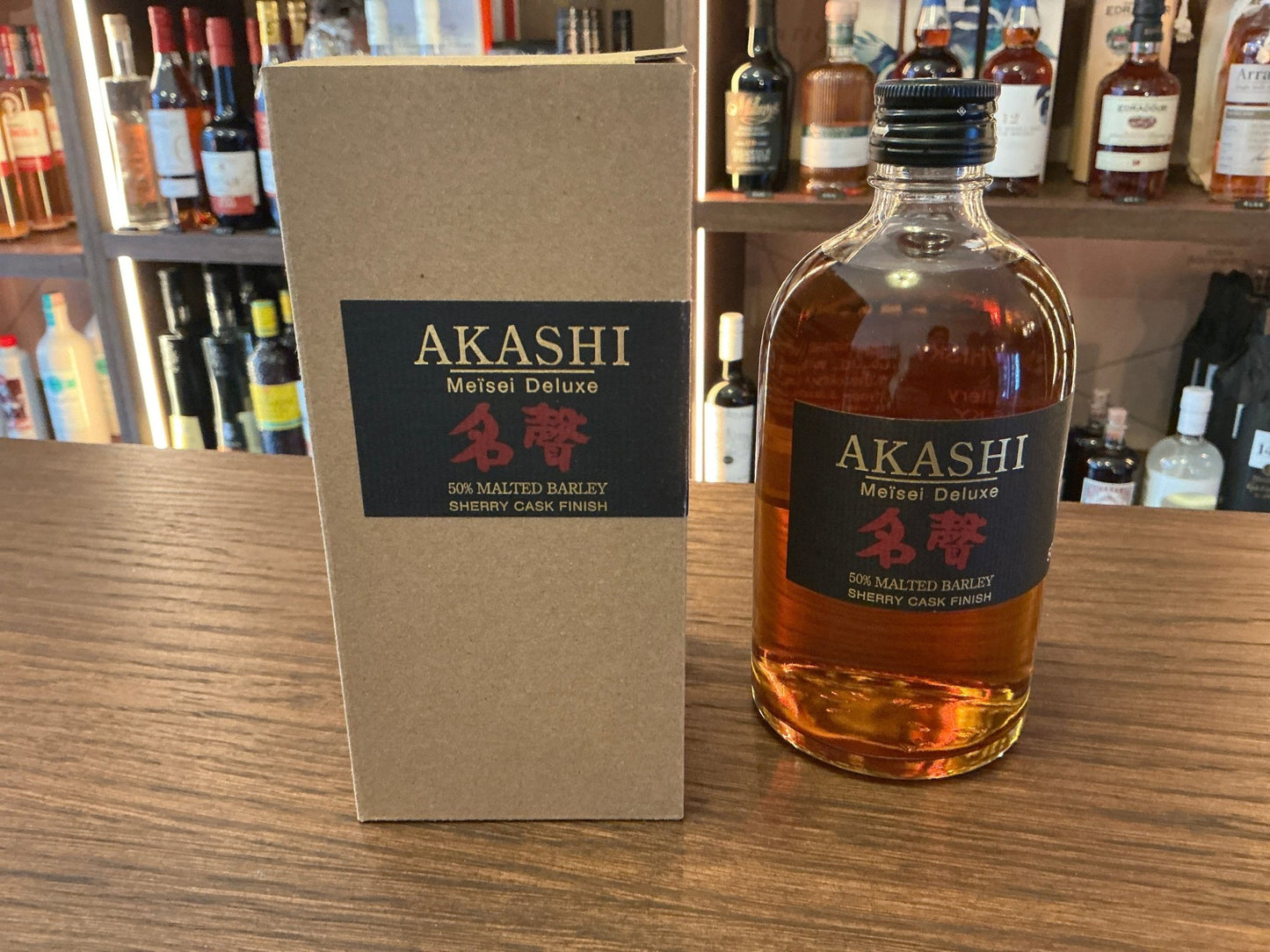 Akashi Meisei Deluxe Sherry Cask Japanese whisky bottle with amber liquid next to premium branded tan box on wooden shelf.