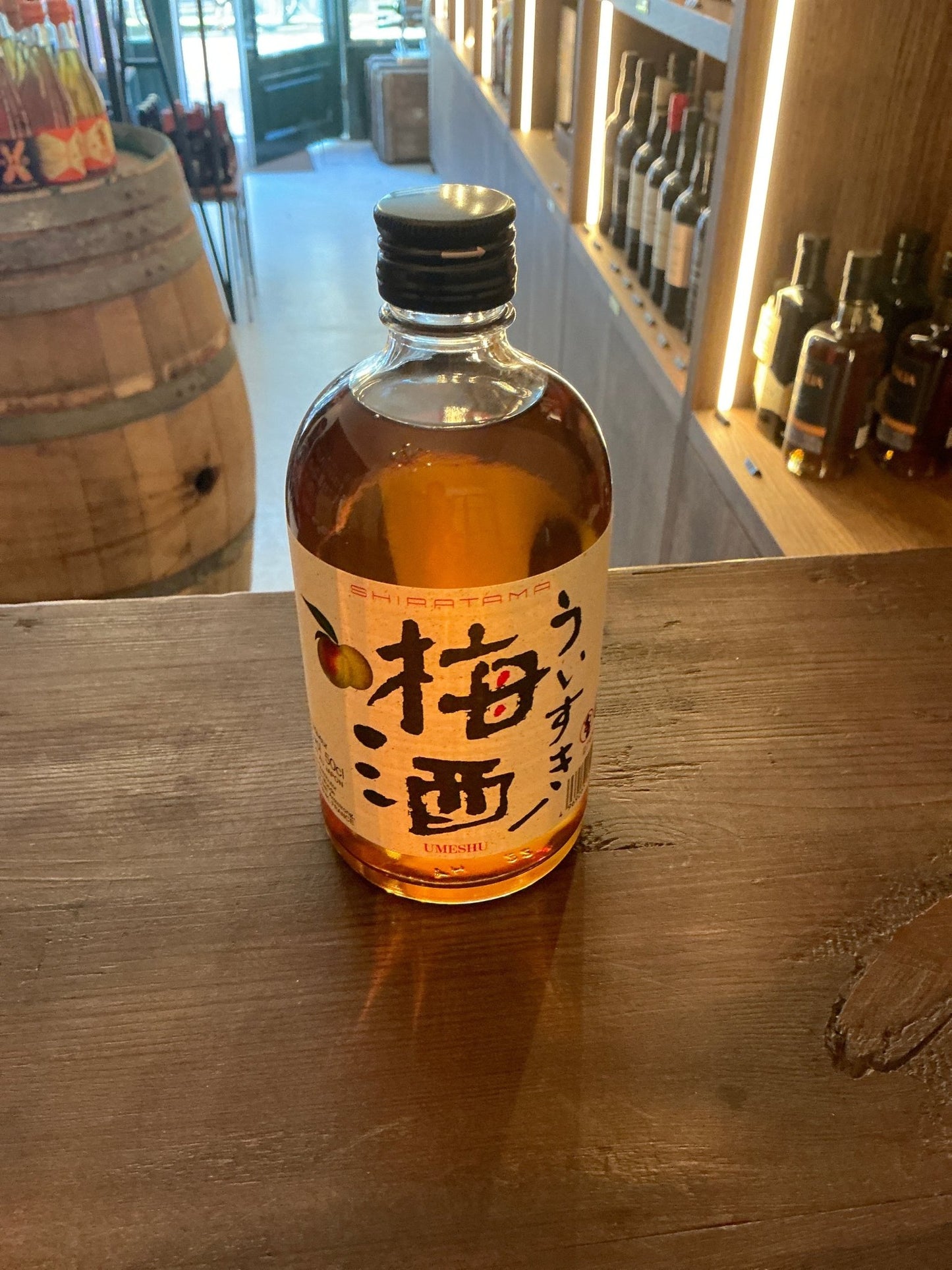 Akashi Umeshu Plum Whisky Liqueur bottle with amber liquid, black cap, and Japanese calligraphy label on wooden surface,.
