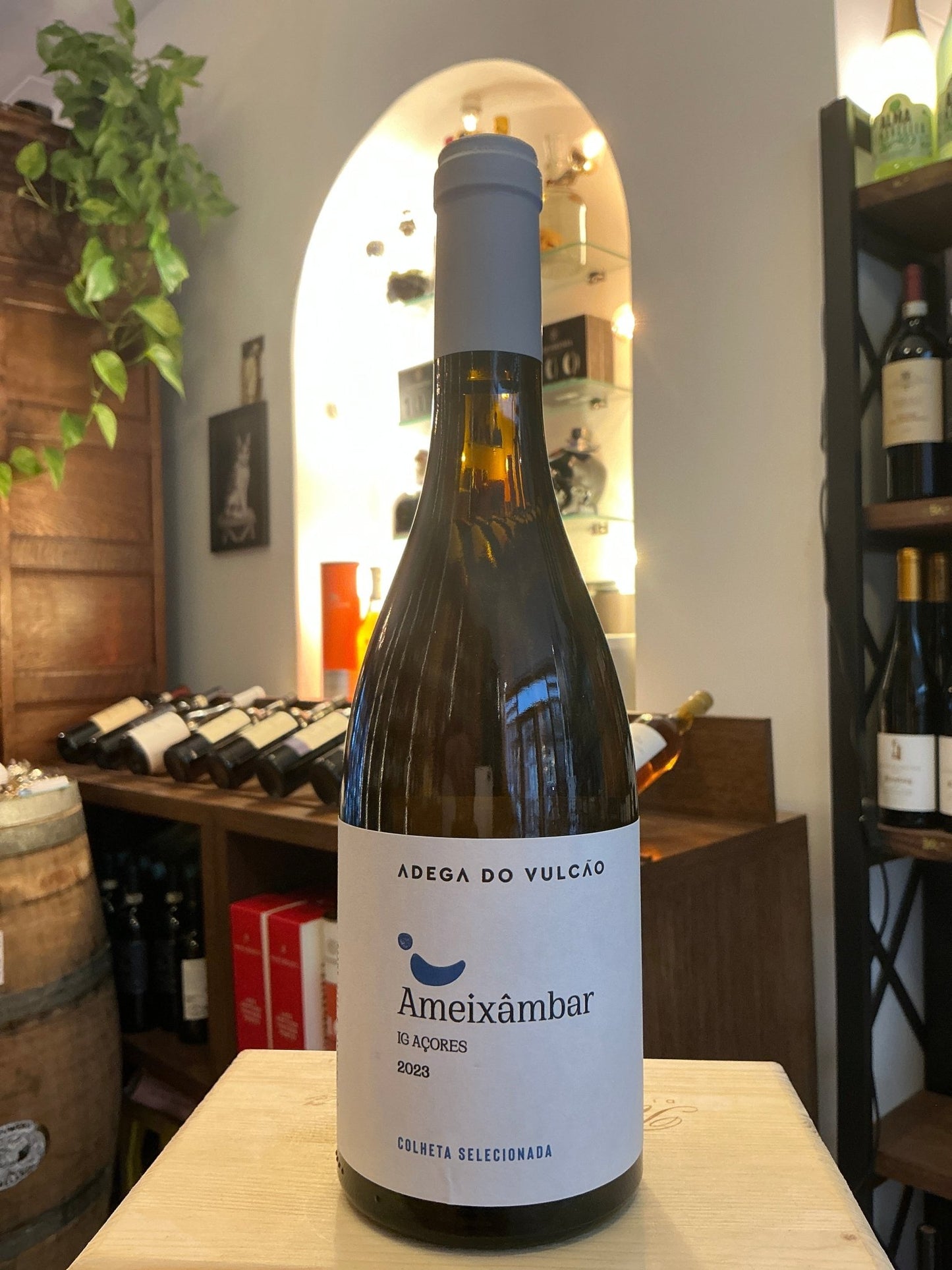 Ameixambar Portuguese white wine bottle with blue cap and minimalist white label, premium artisan spirit displayed indoors.