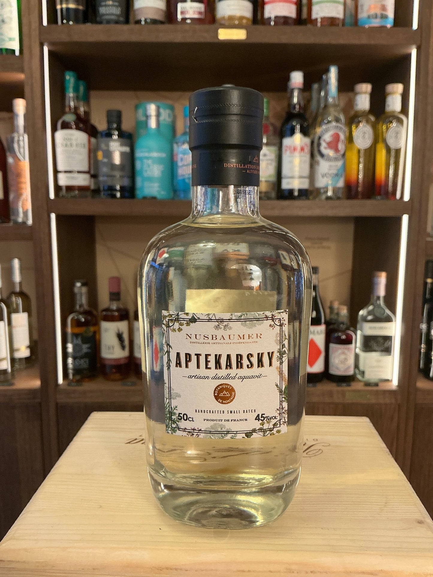 Aptekarsky Aquavit clear glass bottle with black cap, labeled premium distilled botanical spiced spirit on wooden surface.