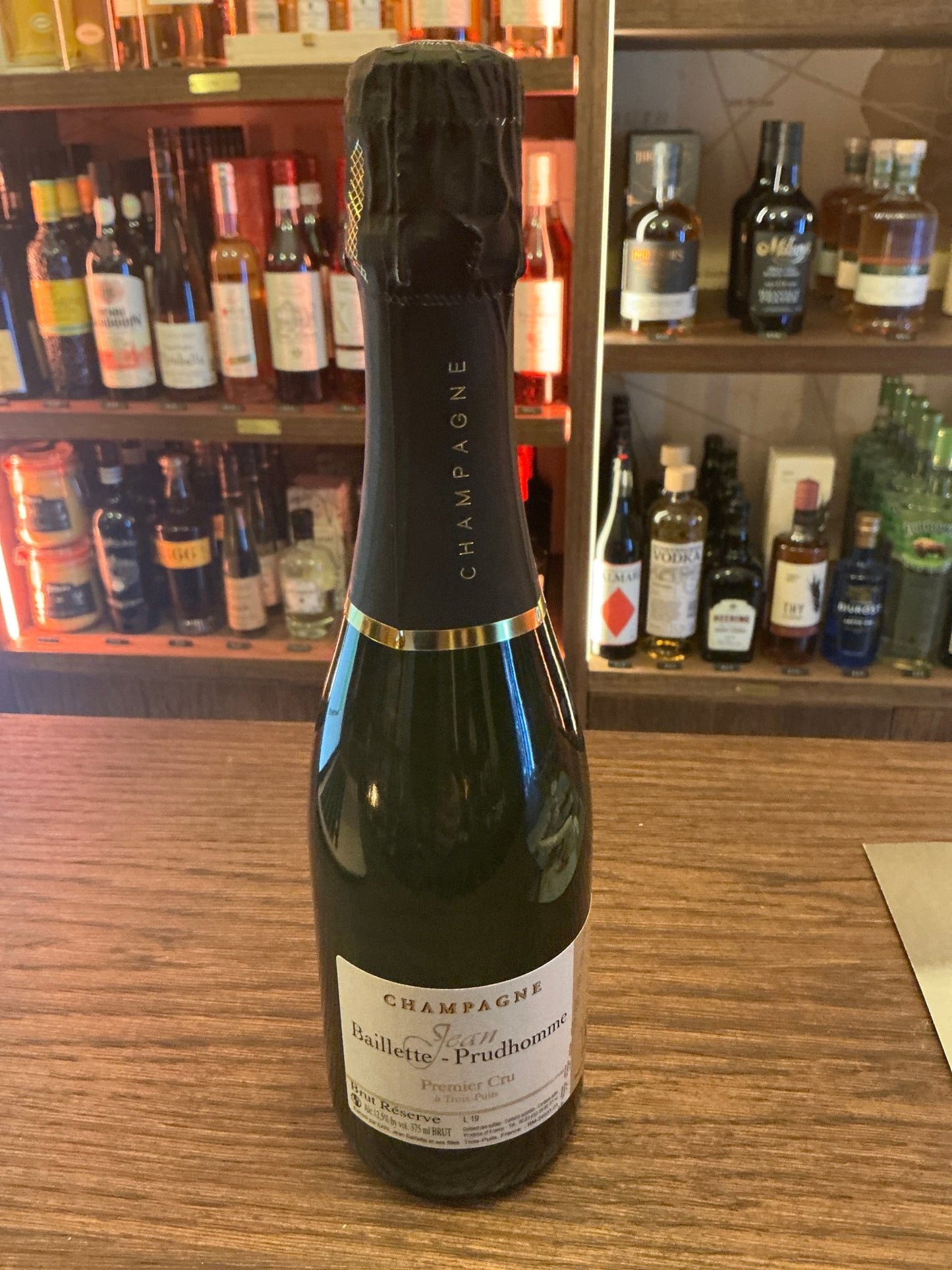 Baillette Prudhomme Champagne 37.5cl bottle with black foil top on wooden bar, premium artisan Dutch specialty spirit.