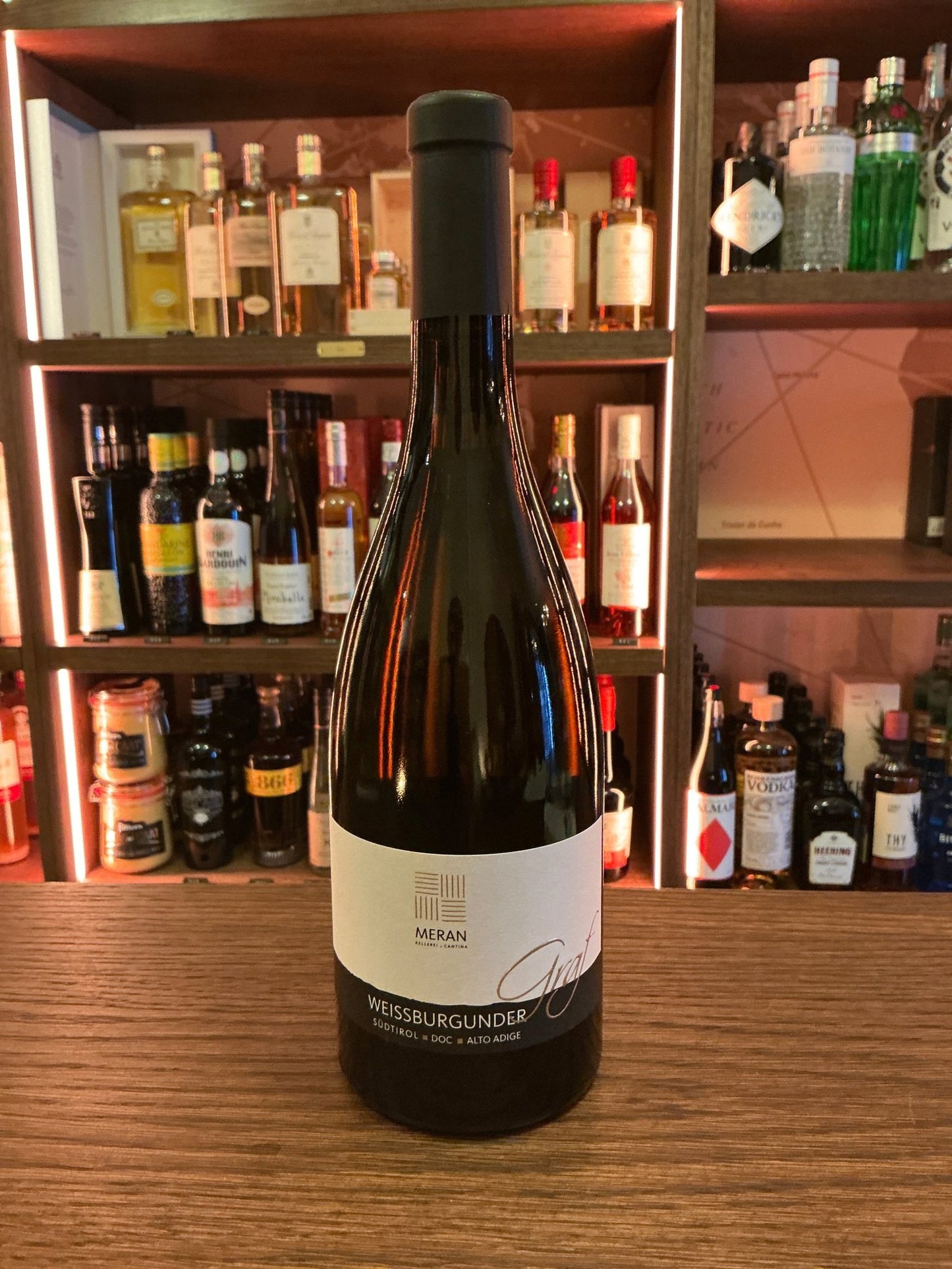 Cantina Merano Weisburgunder Graf von Meran artisan white wine bottle with minimalist label on wooden bar, surrounded by.