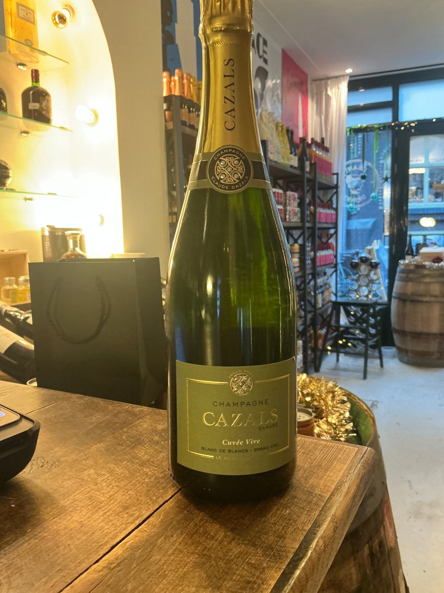 Tall green glass bottle of Cazals Champagne Cuvée Vive with gold foil neck and pale green label on a wooden surface in a.