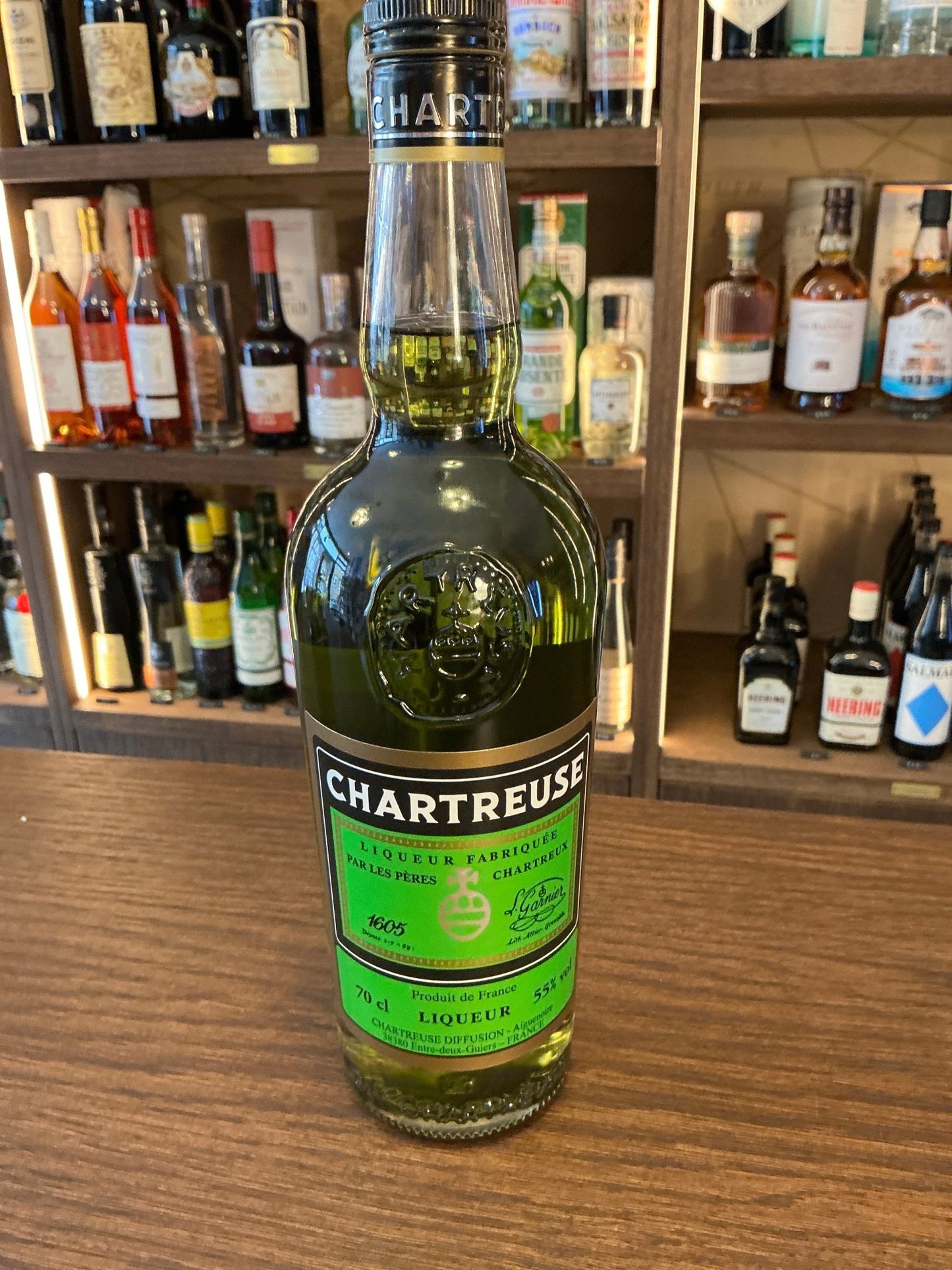Chartreuse green herbal liqueur bottle with botanical, spiced flavors on wooden bar shelf.