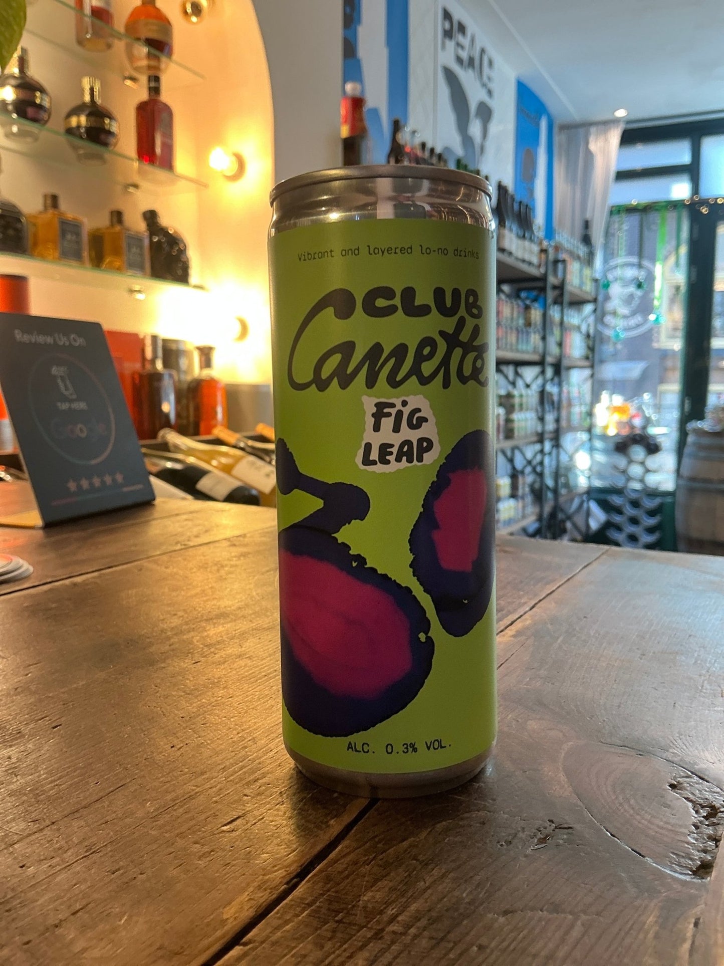 Tall slim Club Canette Fig Leap non-alcoholic aperitif bottle with bright yellow label and bold purple fig illustration on.
