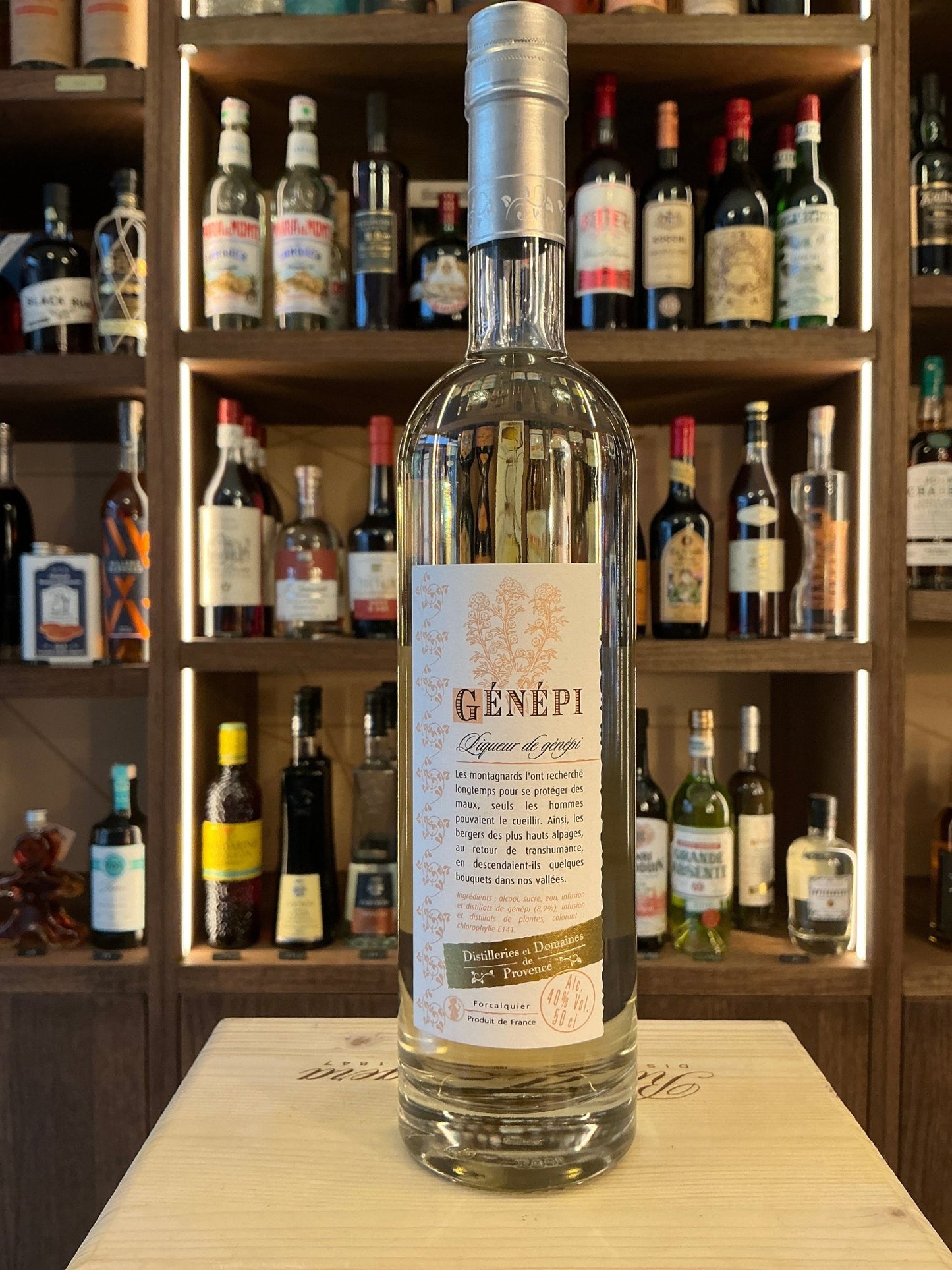 Tall clear bottle of D.D. Provence Génépi herbal liqueur with detailed label, premium artisan botanical spirit on wooden.