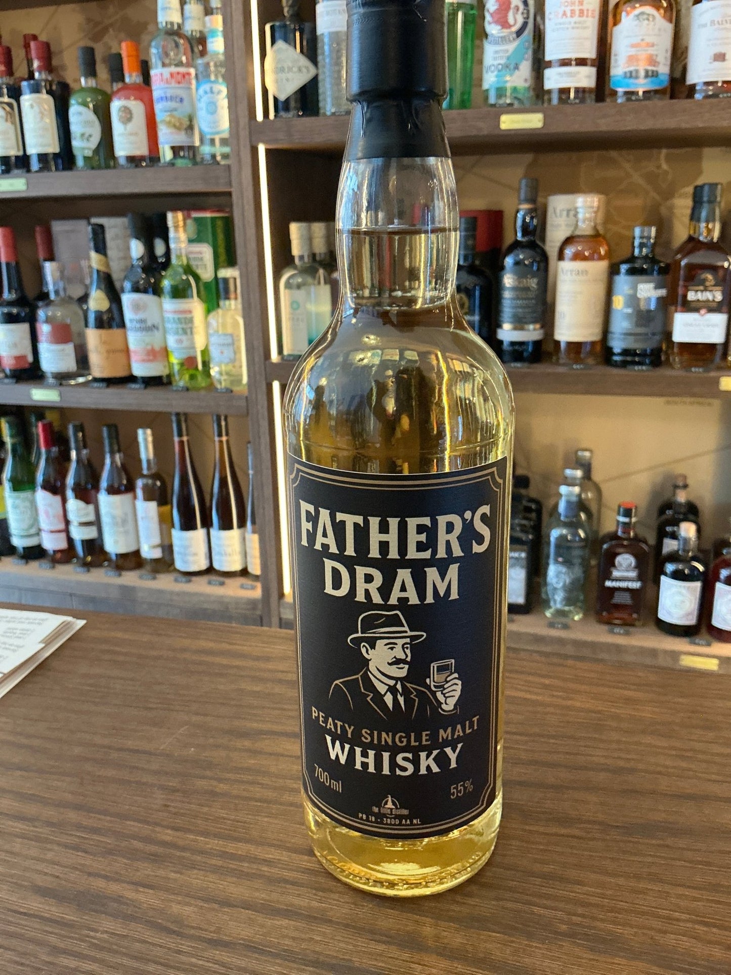 Father’s Dram Peaty Single Malt Whisky bottle with black label, aged premium distilled artisan spirit on wooden bar counter.