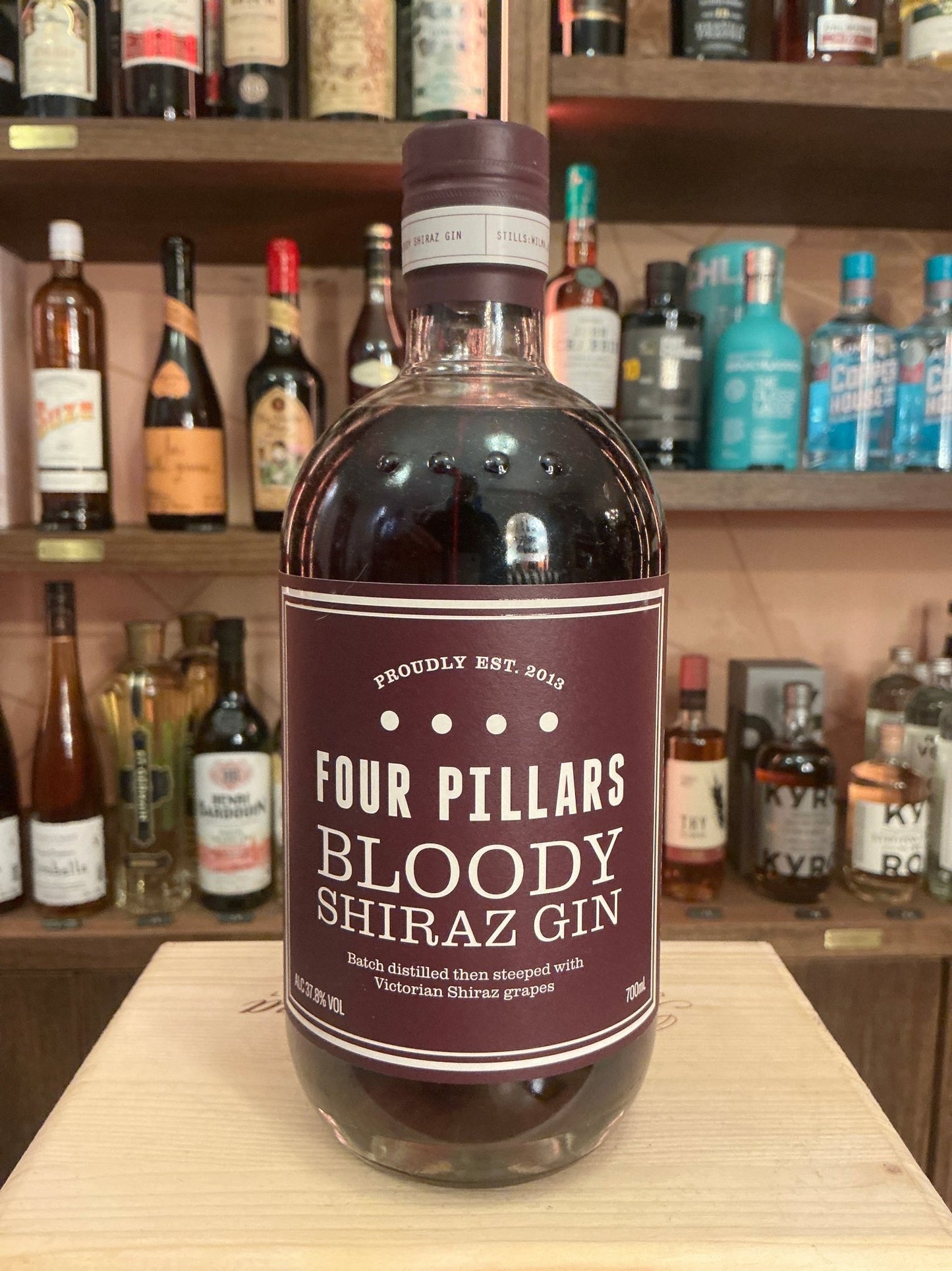 Four Pillars Bloody Shiraz Gin bottle with deep red label, artisan small batch botanical gin displayed on wooden shelf among .