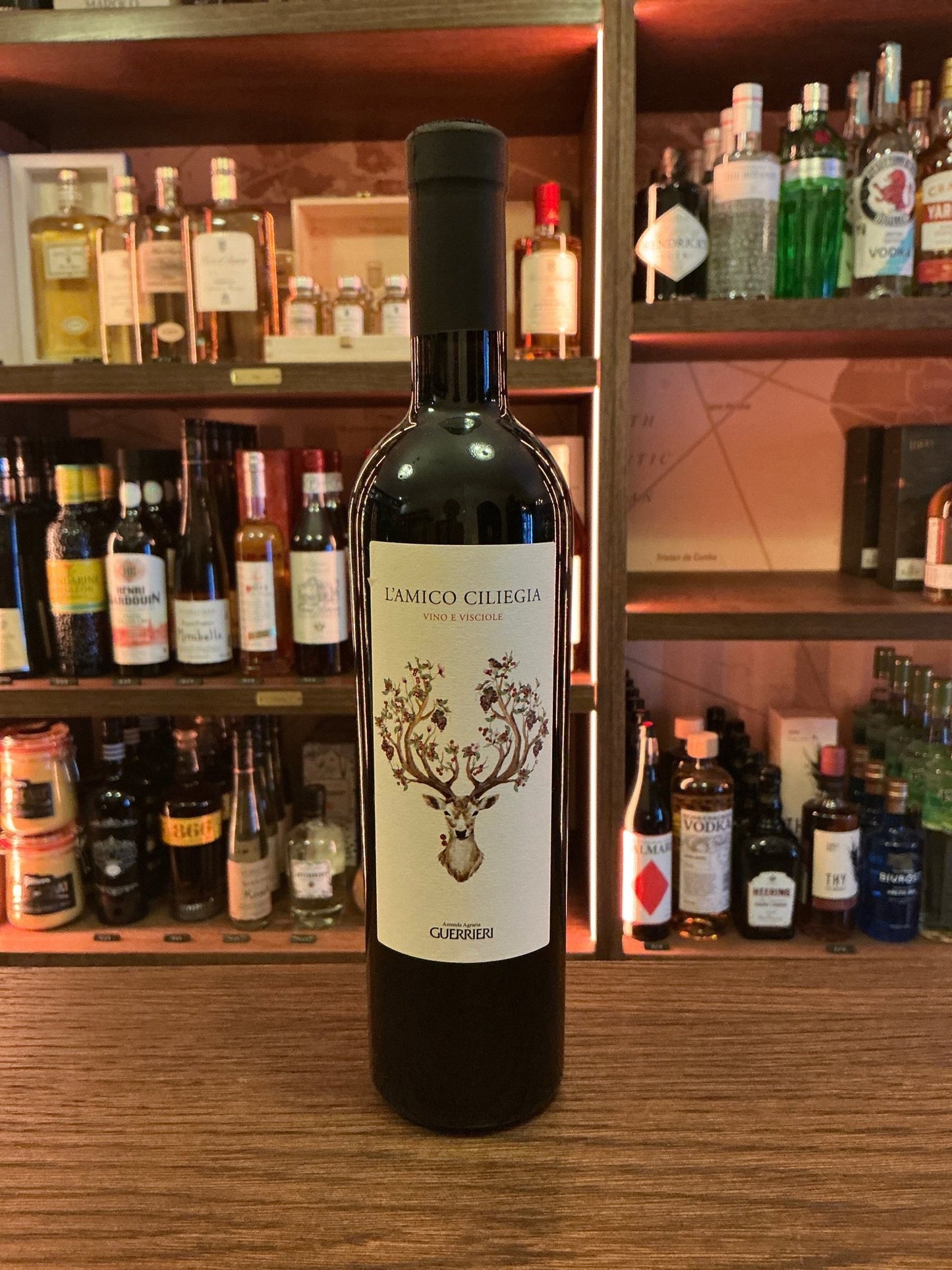 Guerrieri L’Amico Ciliegio Italian red wine bottle with elegant botanical-themed label on wooden bar counter among premium.
