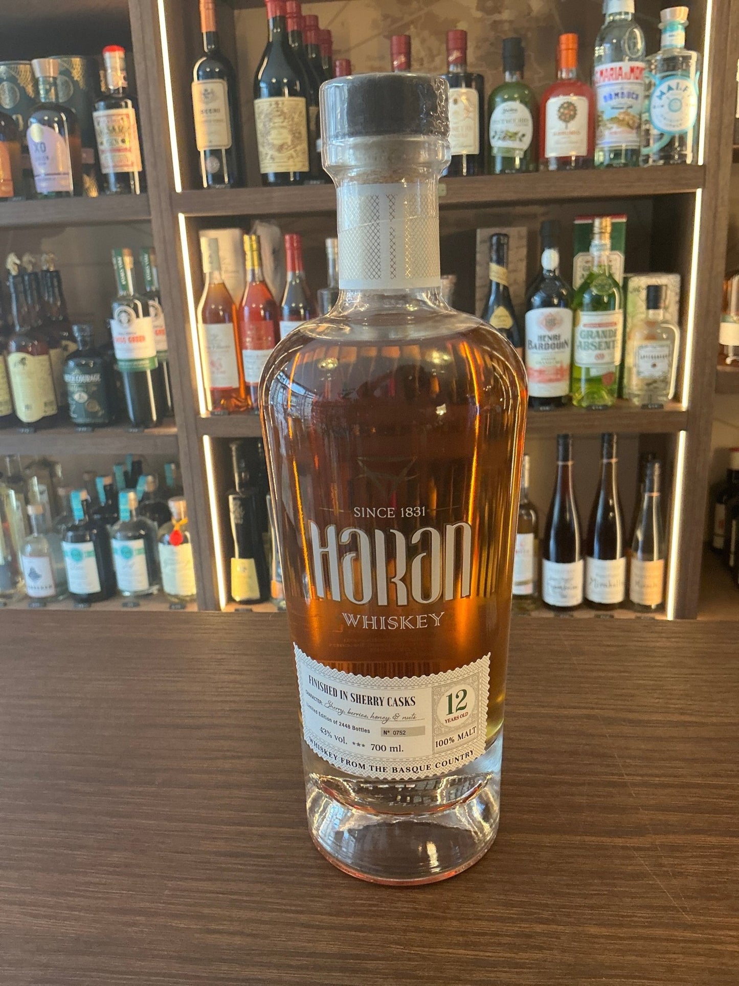 Tall clear glass bottle of Haran 12 Year Old Basque Malt whisky with amber liquid, premium artisan spirits label, aged and.