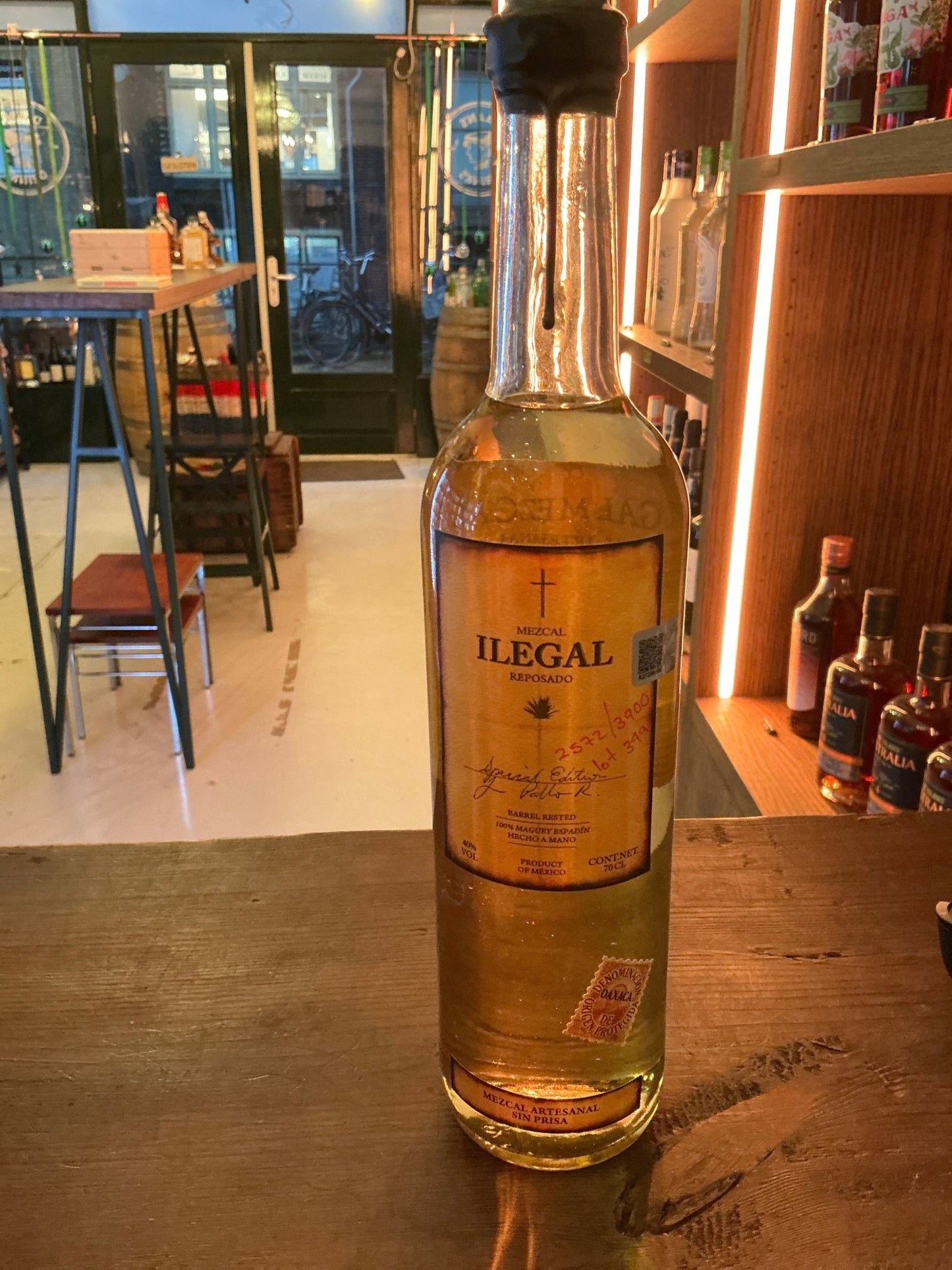 Illegal Mezcal premium small batch artisan mezcal bottle with golden amber liquid on wooden counter.