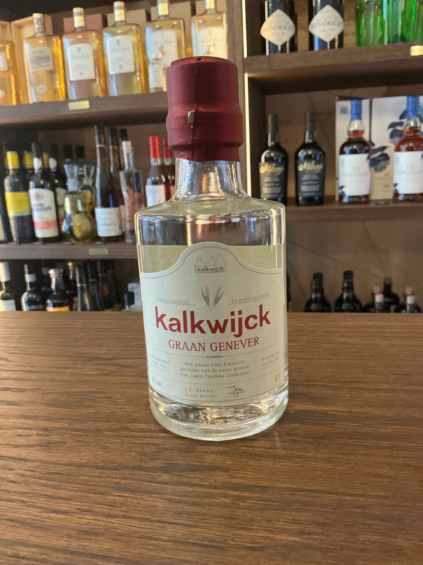 Clear glass bottle of Kalkwijck Graan Genever with maroon cap and white label, premium Dutch artisan spirit distilled with.