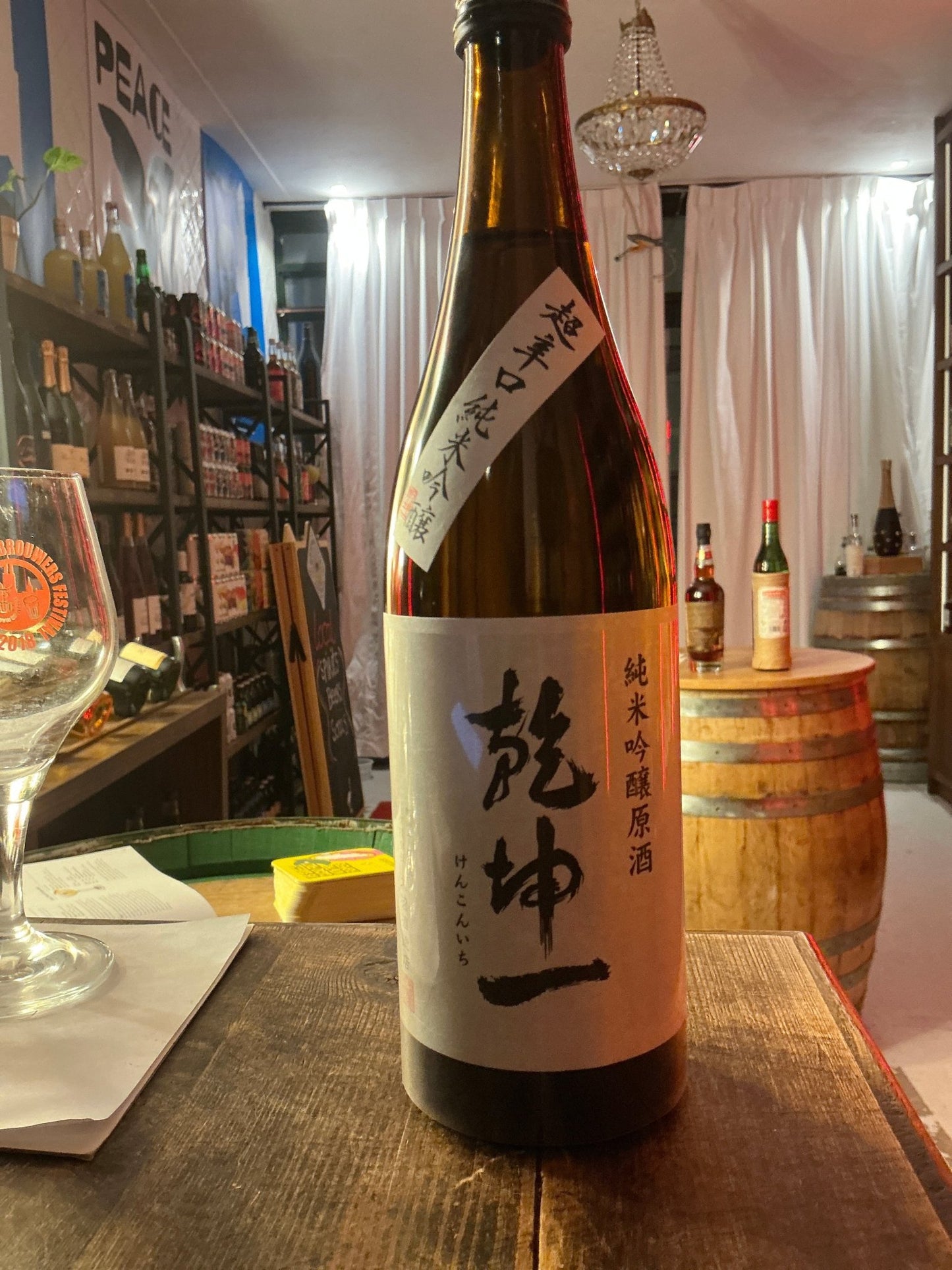 Tall brown bottle of Kenkonichi Junmai Gingo Chokara sake with white label featuring Japanese characters, displayed on.