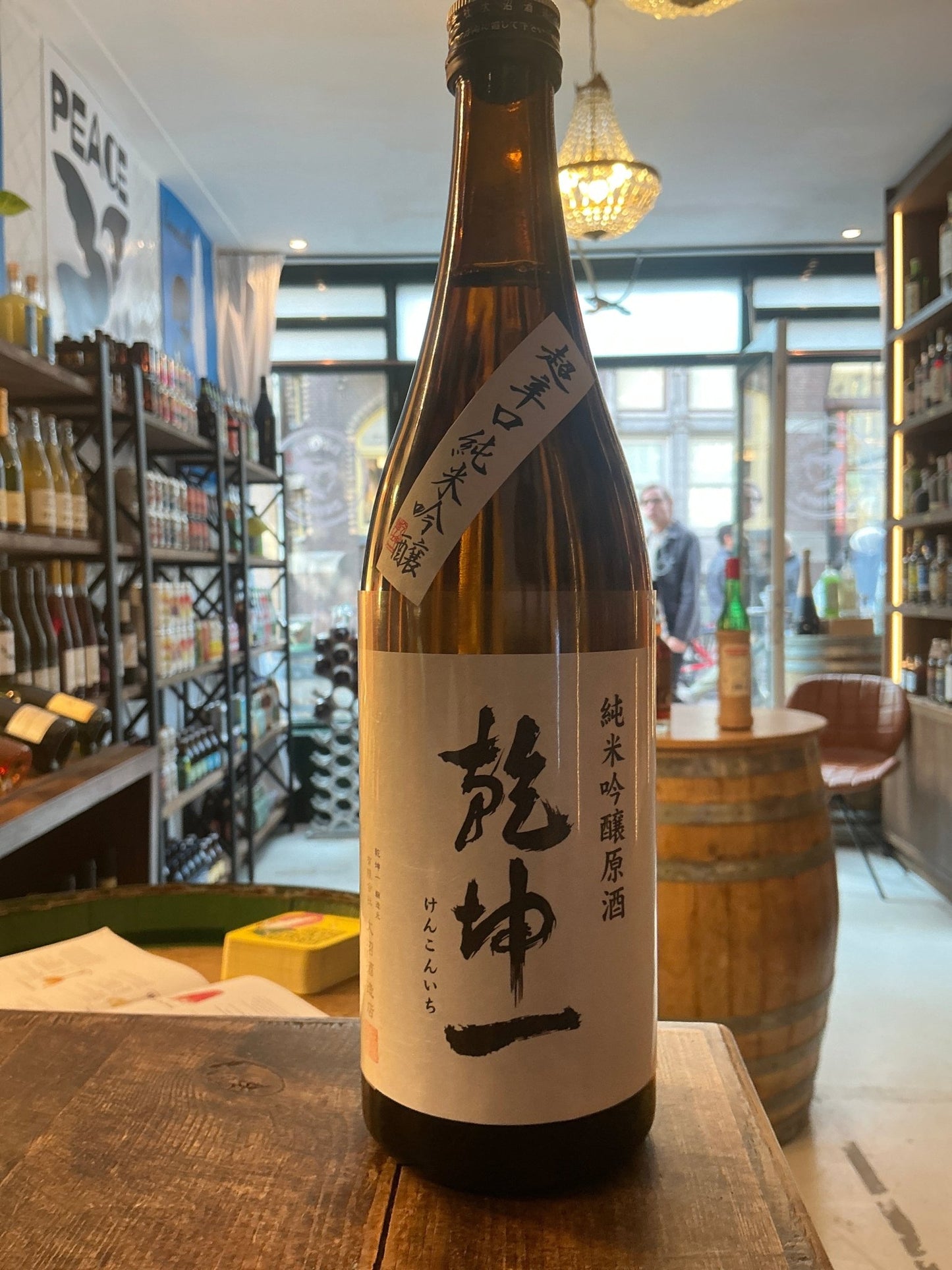 Brown glass bottle of Kenkonichi Tokubetsu Junmai Karakuchi sake with minimalist white label and black Japanese calligraphy, .