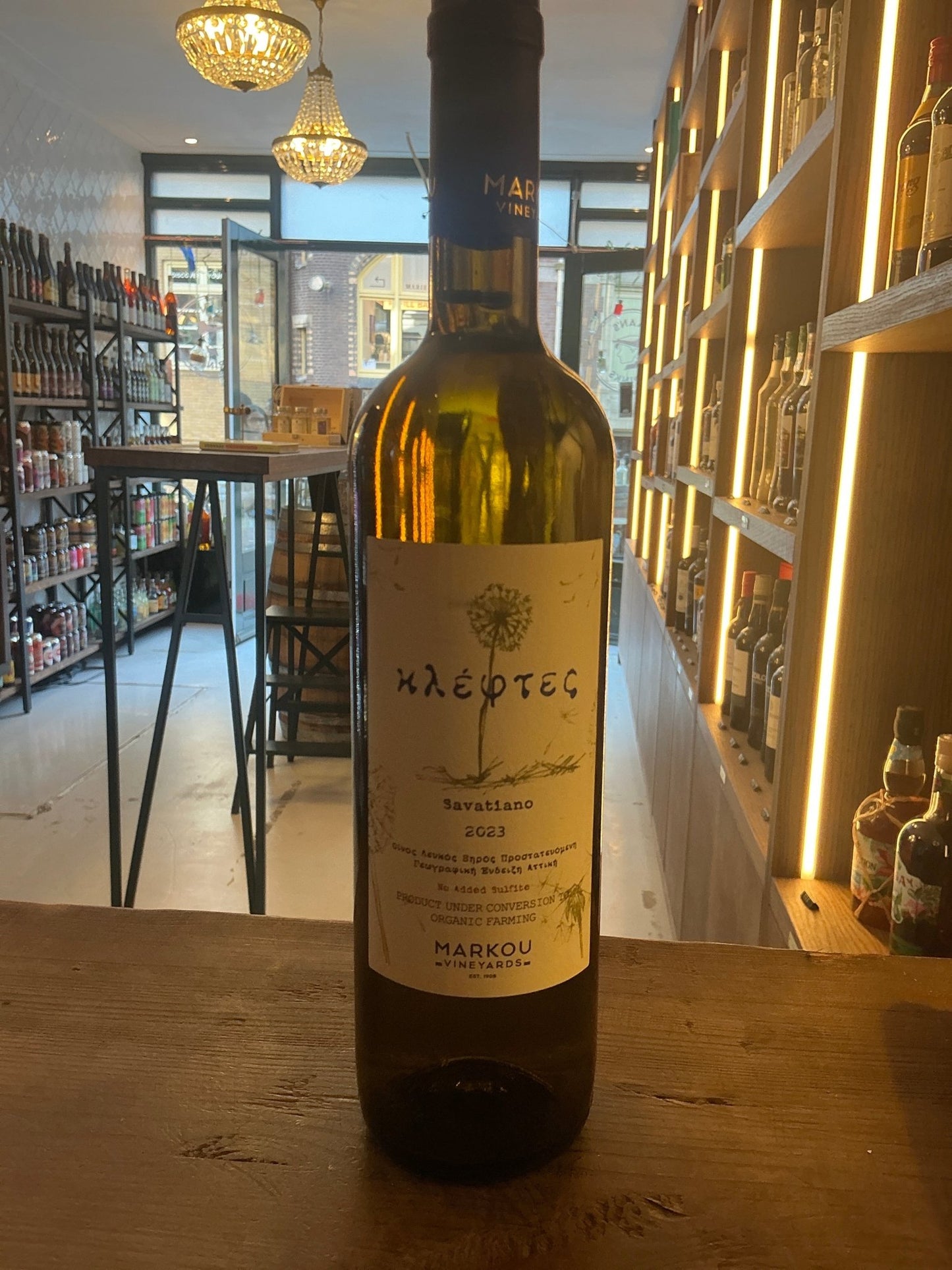 Kleftes 2022 Greek white wine bottle from Markou Vineyards with artisan labeling on wooden table in rustic shop setting.