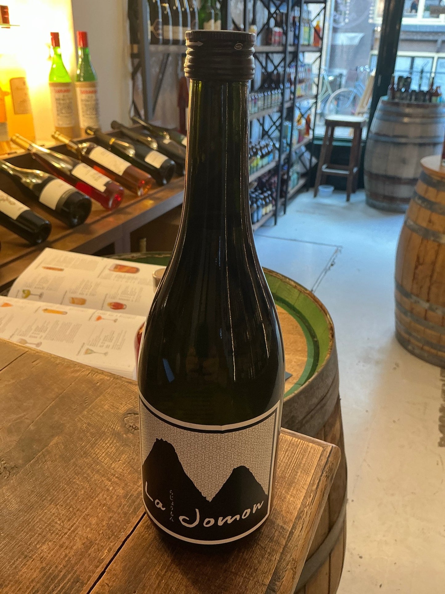 La Jomon Junmai-shu sake bottle with minimalist black and white label on wooden table in artisan spirits shop.