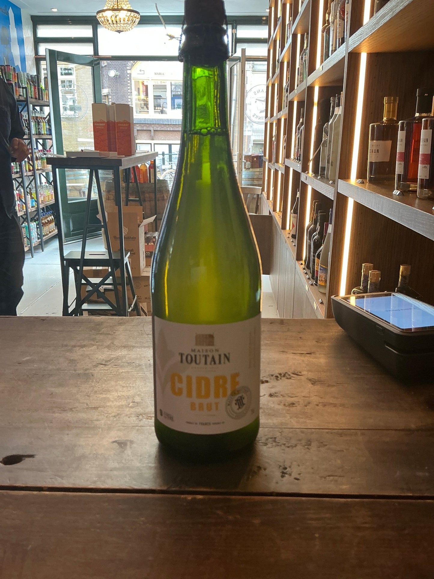 Maison Toutain Cidre Brut bottle with green glass and white label on wooden table, artisan Normandy cider, premium craft.