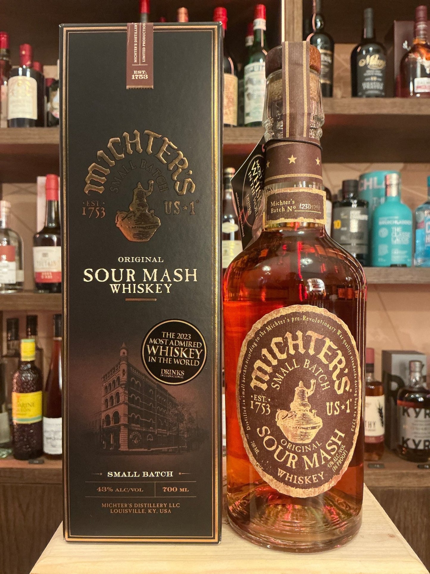 Michter’s Small Batch Sour Mash Whiskey bottle with amber liquid, embossed label, premium aged American bourbon beside black .