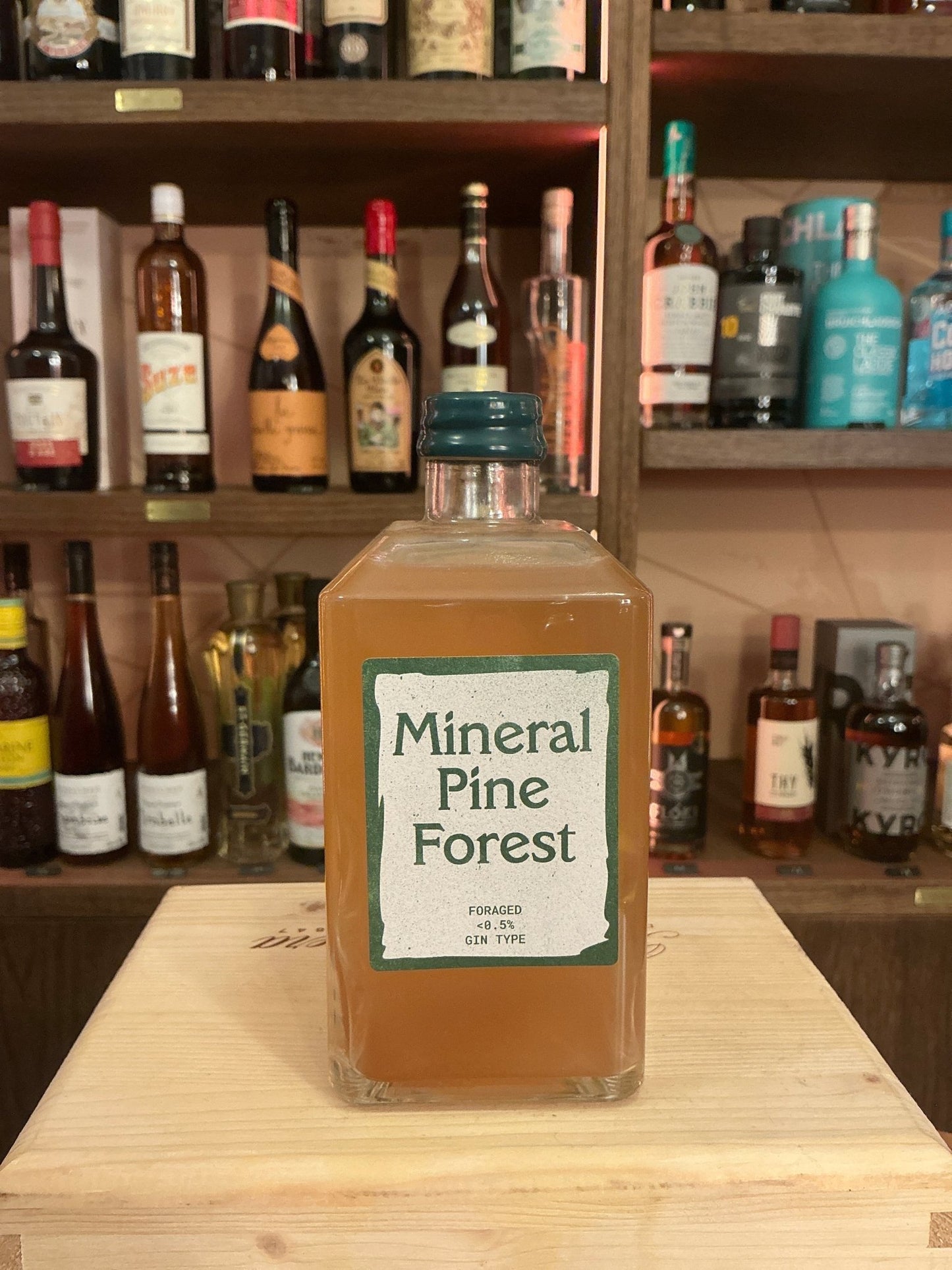 Square glass bottle of Mineral Pine Forest alcohol-free botanical spirit with green label and dark green cap on wooden.