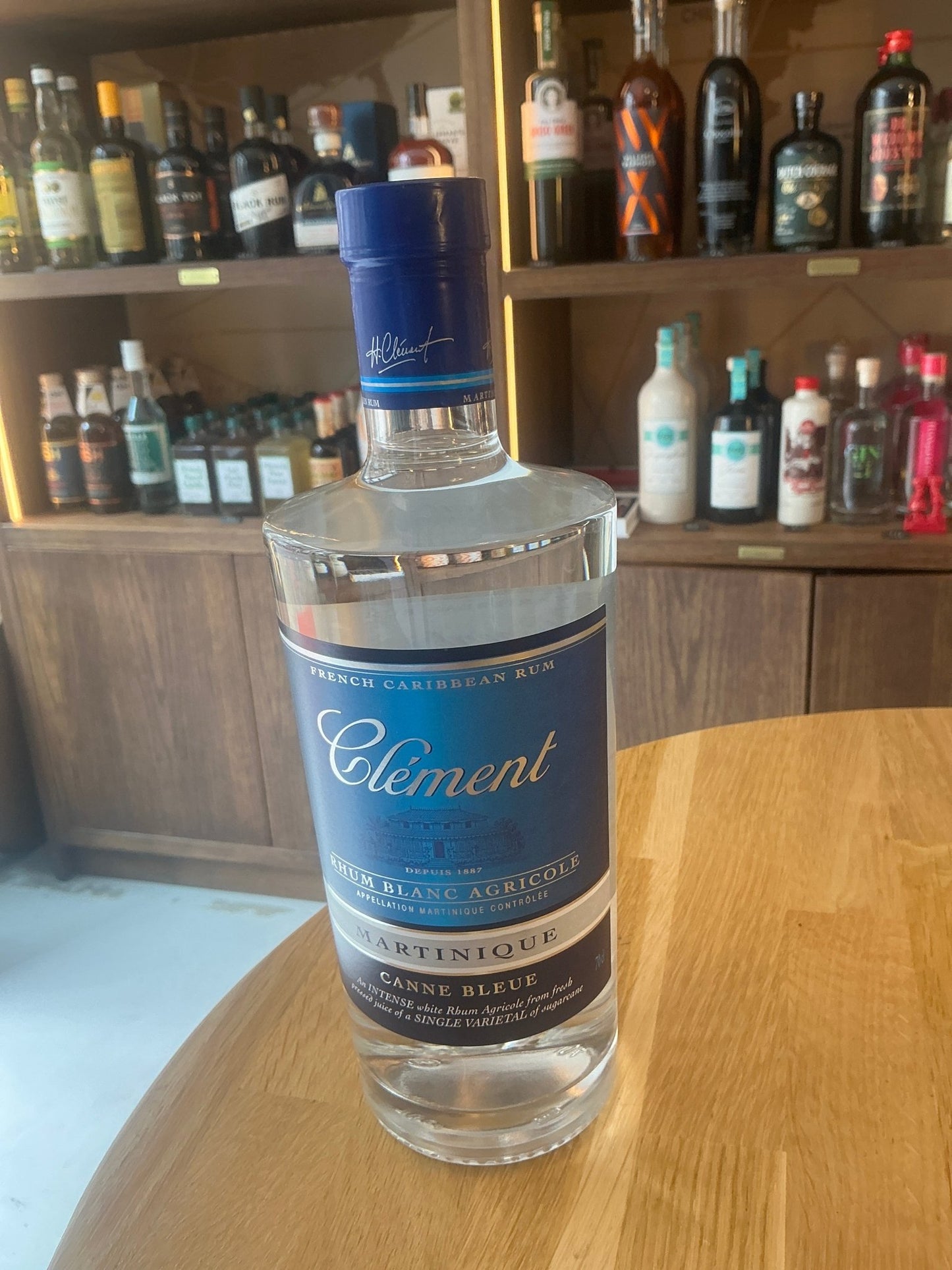 Clear glass bottle of Rhum Clément Canne Bleue white rum with blue label and cap, artisan premium small batch spirit on.