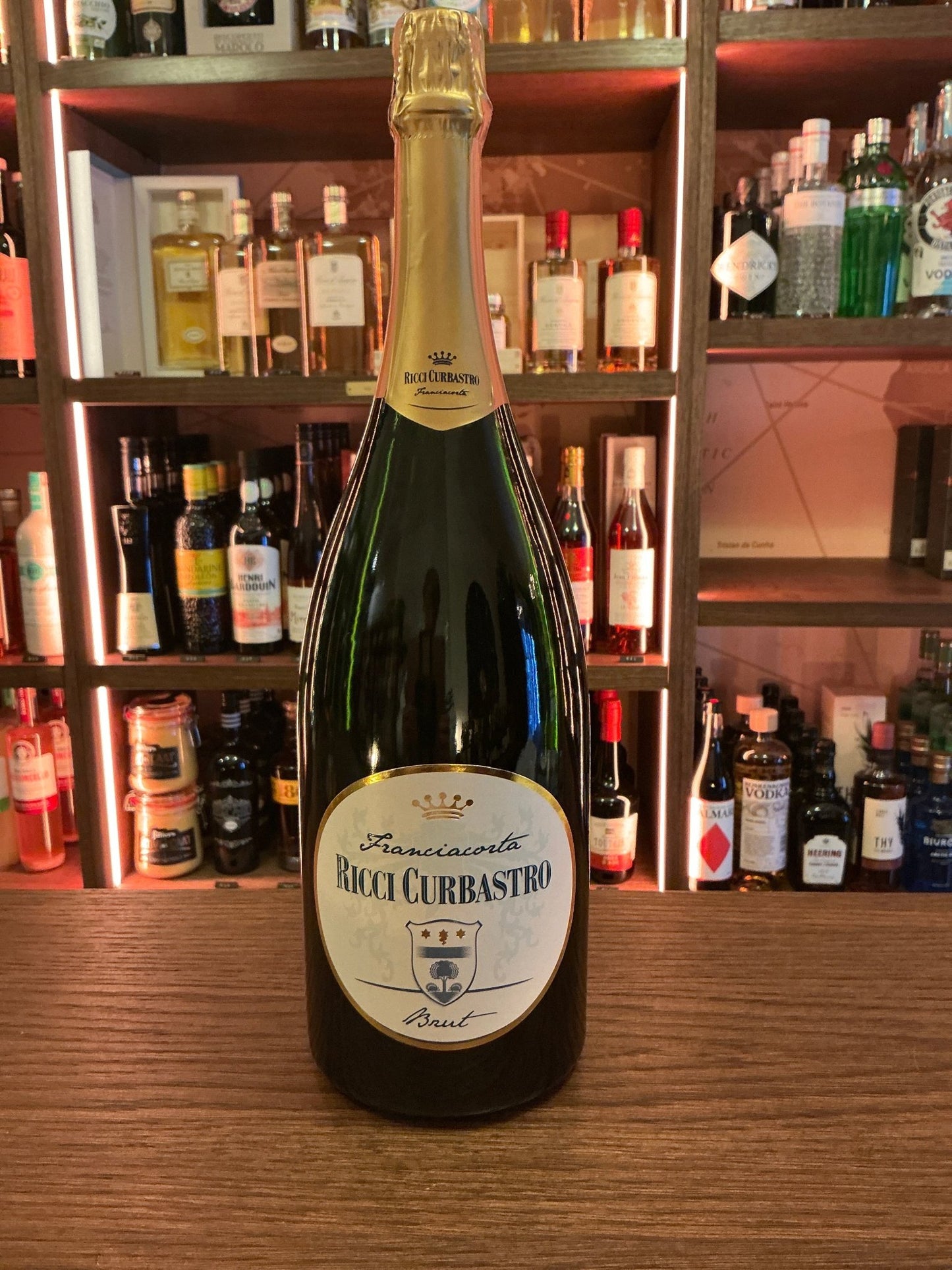 Ricci Curbastro Brut Magnum 1.5L bottle of premium Italian sparkling wine with gold foil neck label on wooden bar counter,.