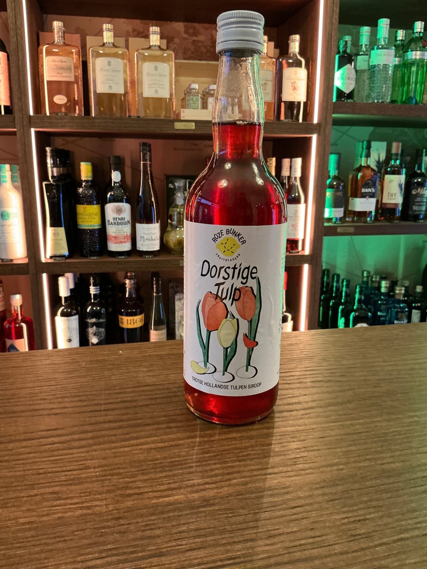 Roze Bunker Dorstige Tulp cordial bottle with red liquid, botanical flower design, artisan Dutch specialty spirits on wooden .