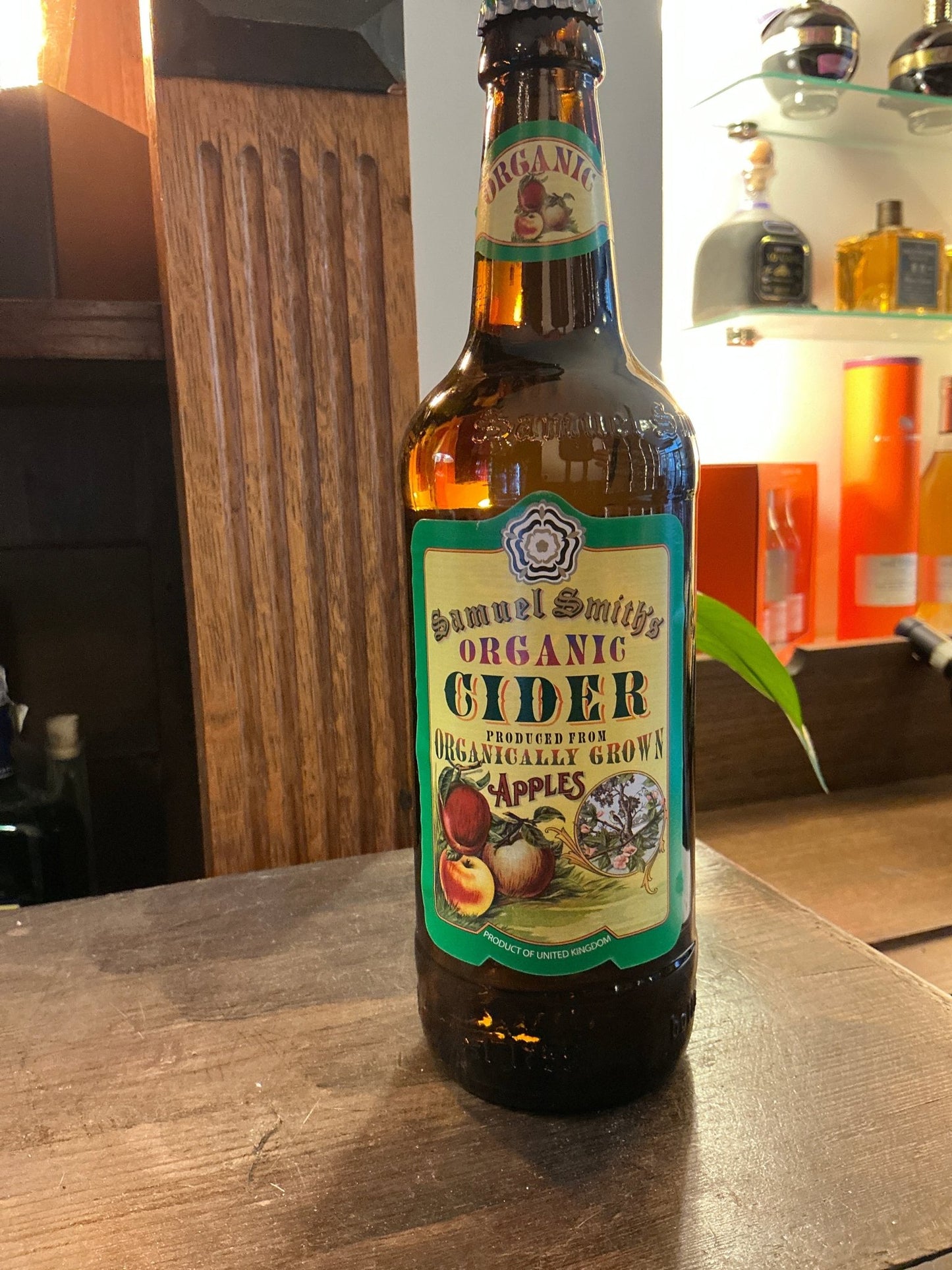 Samuel Smith's Organic Cider bottle with green and cream label featuring apples and botanical design, placed on wooden.