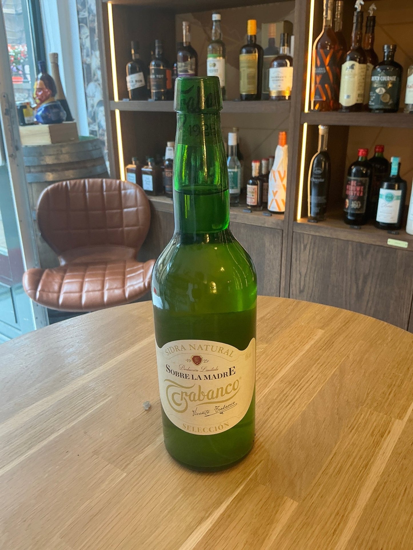 Green glass bottle of Trabanco Sidra Natural Spanish cider with white and gold label on wooden table, premium artisan small.