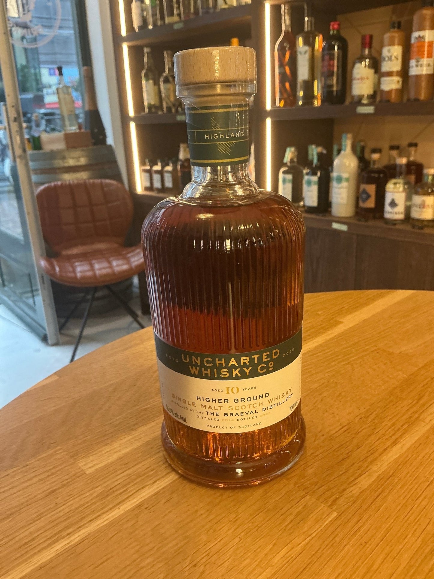 Uncharted Whisky Higher Ground 10 Year Braeval Single Malt amber bottle with ribbed glass and gold cap on wooden bar counter.