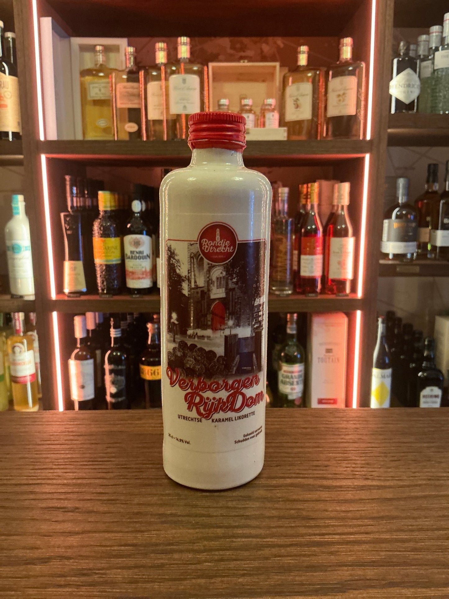Tall white ceramic bottle of Verborgen Rijkdjom Karamel Likorette caramel liqueur with red cap and vintage Dutch design on.