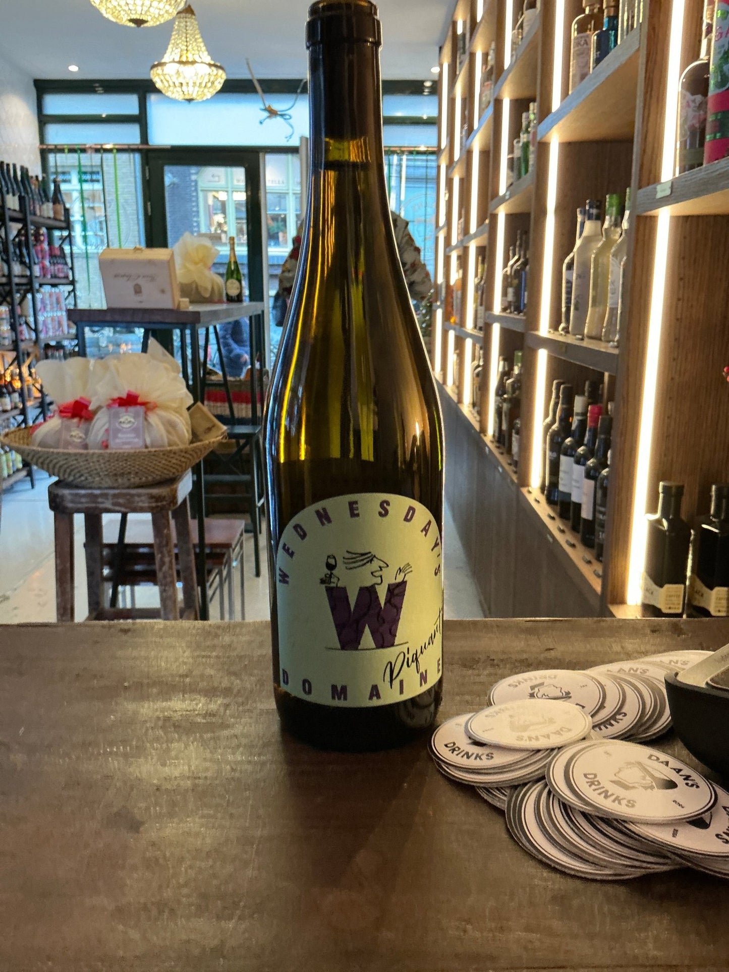 Wednesday’s Piquante non-alcoholic wine bottle with minimalist white label and large red "W" emblem on wooden counter in.