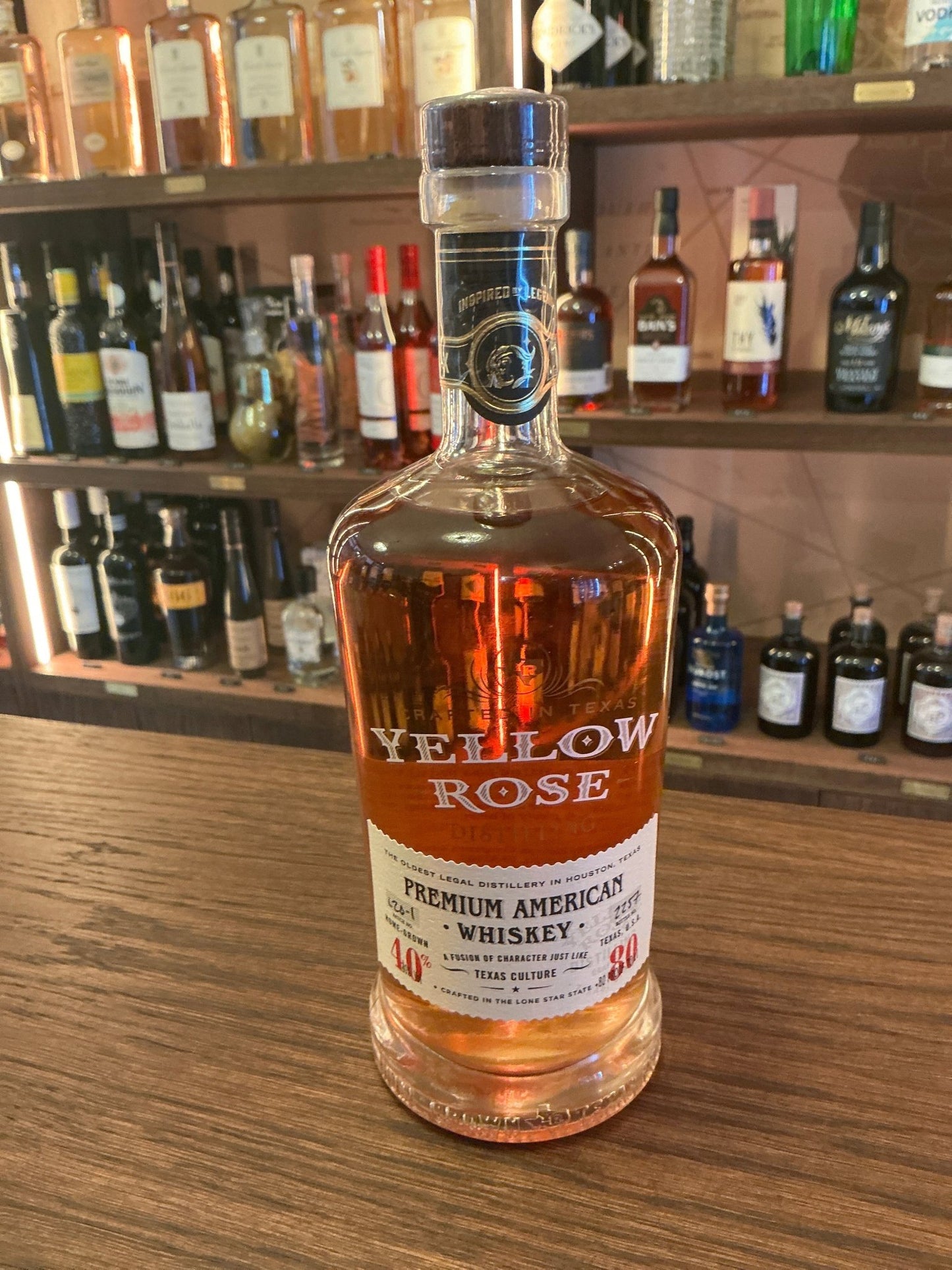 Yellow Rose Whiskey bottle with amber aged bourbon, labeled premium American small batch artisan distilled spirit on wooden.