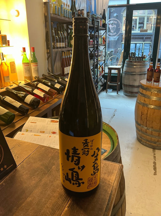 Tall dark glass bottle of Bakkan Nasake Shima Shochu with yellow label featuring Japanese calligraphy, artisan specialty.