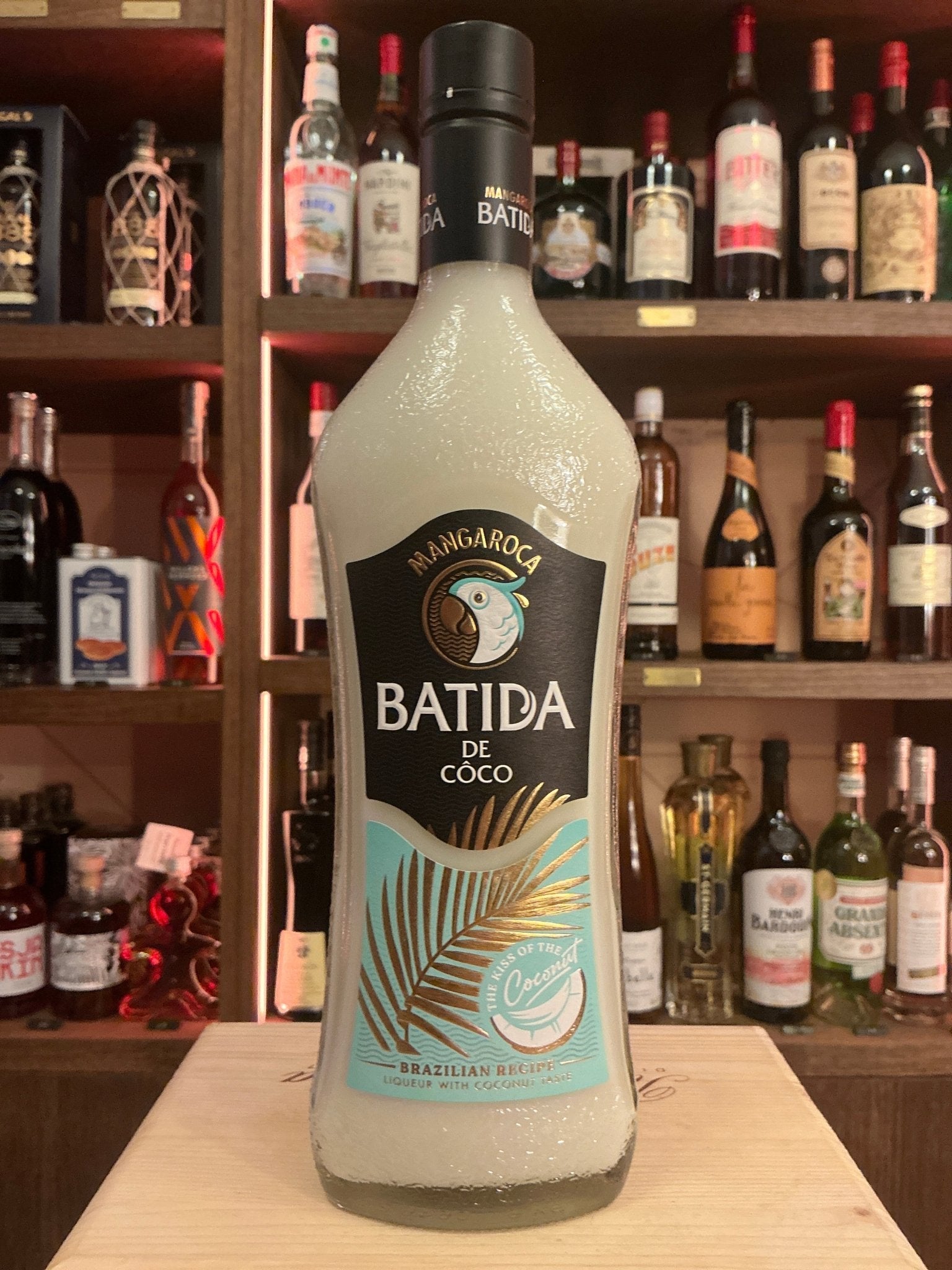 Tall frosted bottle of Batida de Coco cream liqueur with black cap and tropical palm leaf design, displayed on countertop.