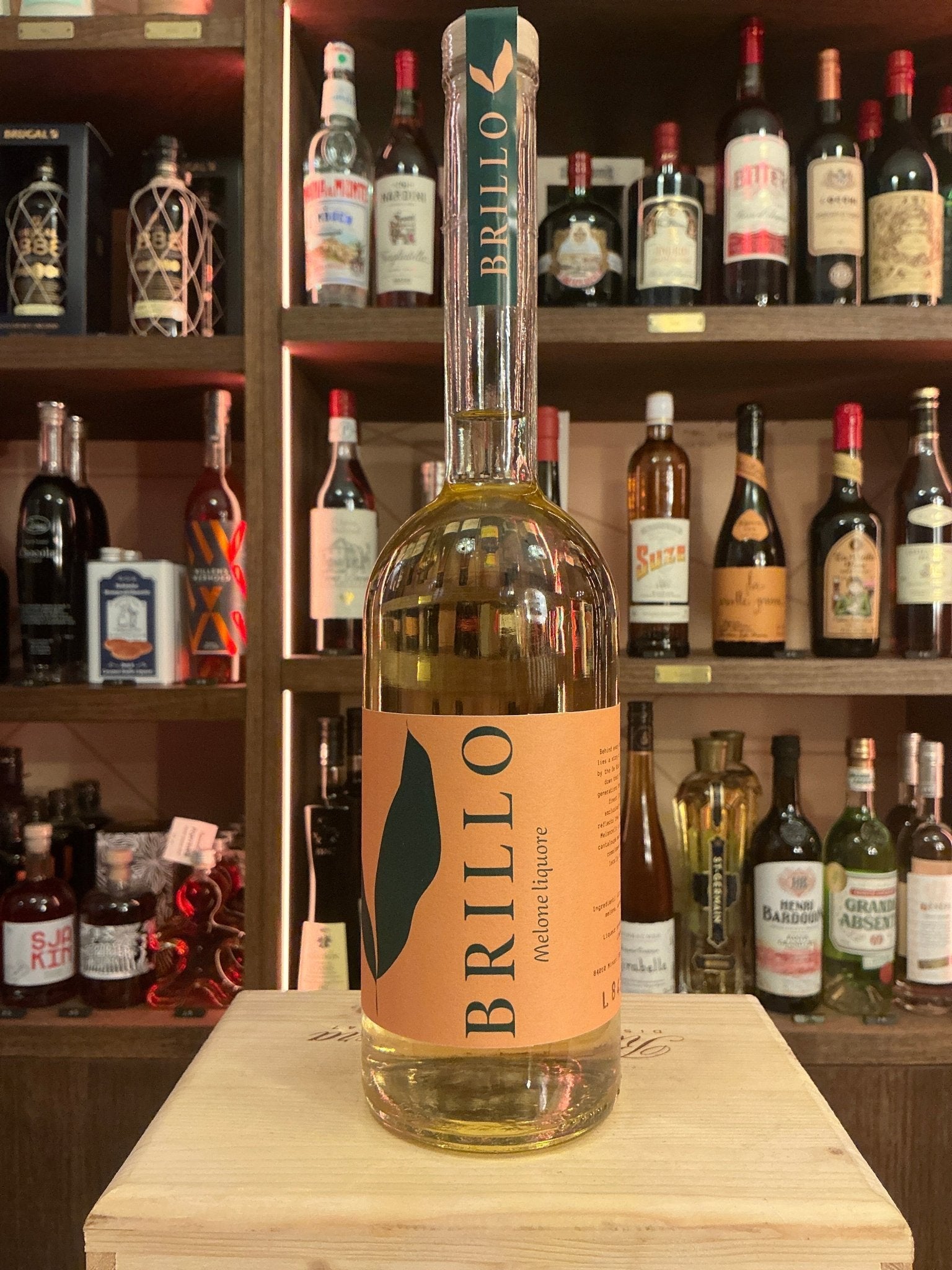 Brillo Meloncello artisanal melon liqueur in clear glass bottle with orange label, premium specialty spirits on wooden.