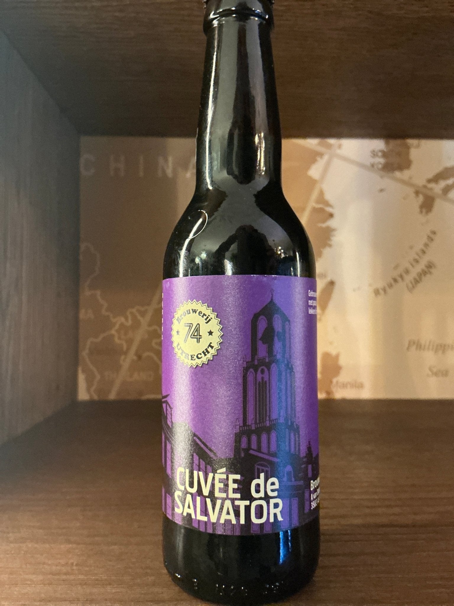 Dark glass bottle of Brouwerij 74 Cuvée de Salvator Belgian Quadrupel with purple label featuring a black tower silhouette,.