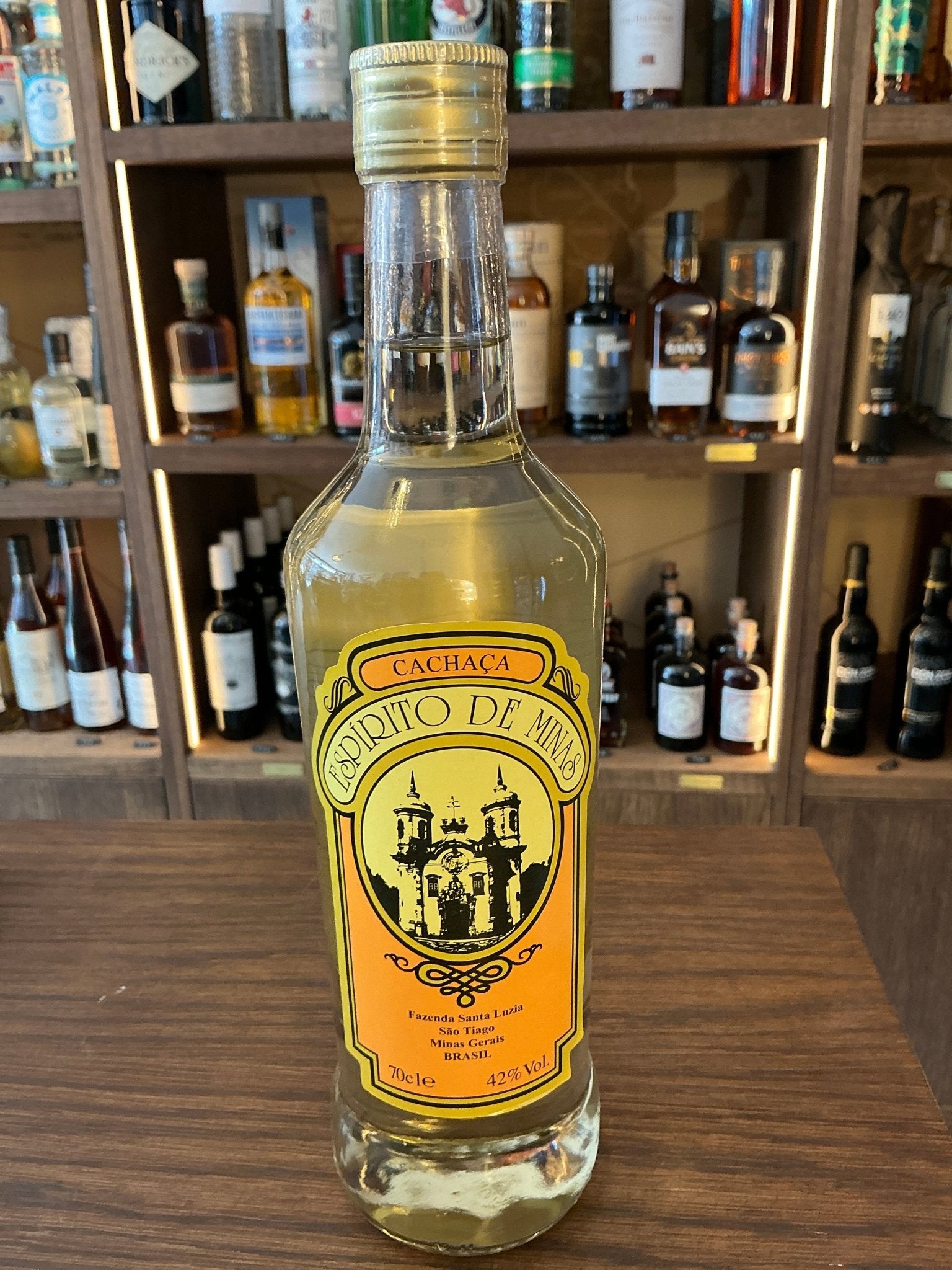 Clear glass bottle of Cachaca Espirito De Minas with orange and yellow label featuring a castle illustration, premium aged.