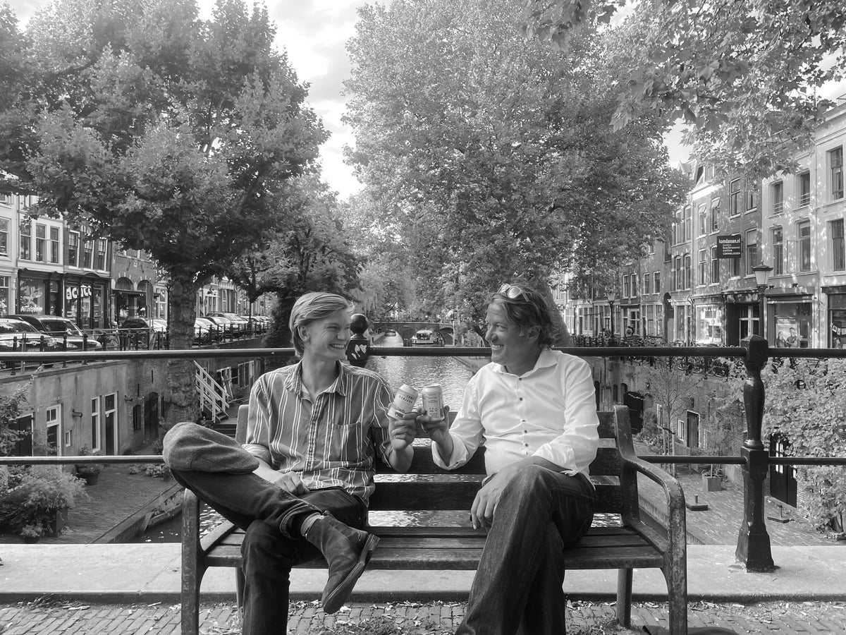Daan and Simon, founders of Daan's Drinks, toasting on a bench by the Oudegracht canal in Utrecht