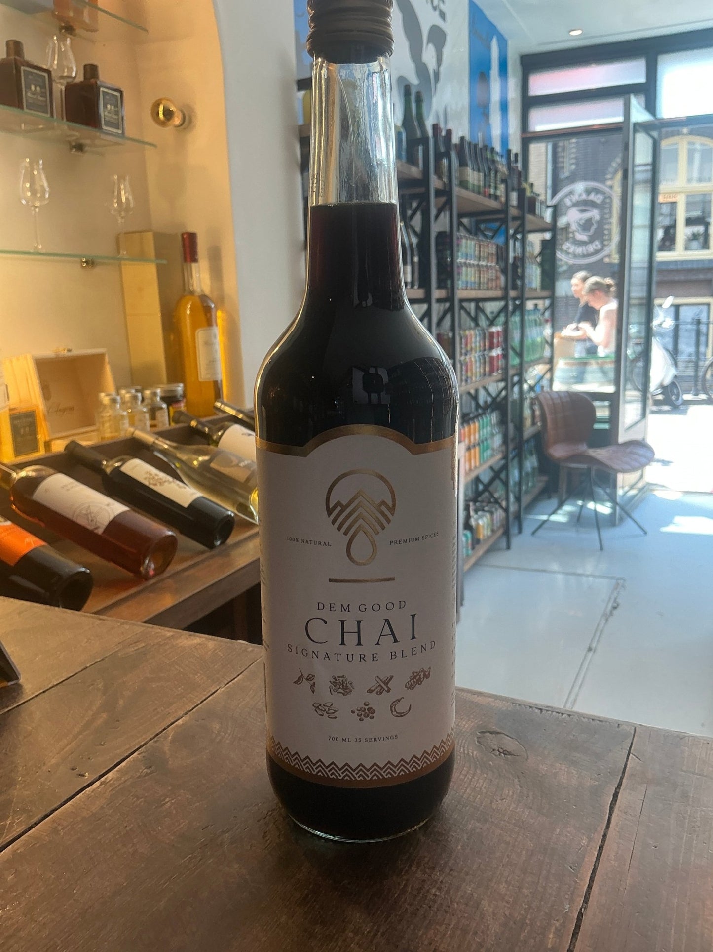 Dem Good Chai artisan botanical spiced tea infusion bottle for specialty spirits on wooden counter in bright rustic store.