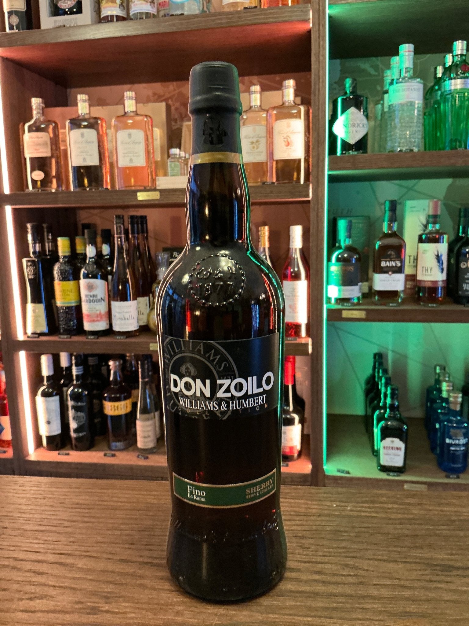 Don Zoilo Fino Sherry bottle with black label and red accents, artisan premium distilled specialty spirit on wooden bar shelf.