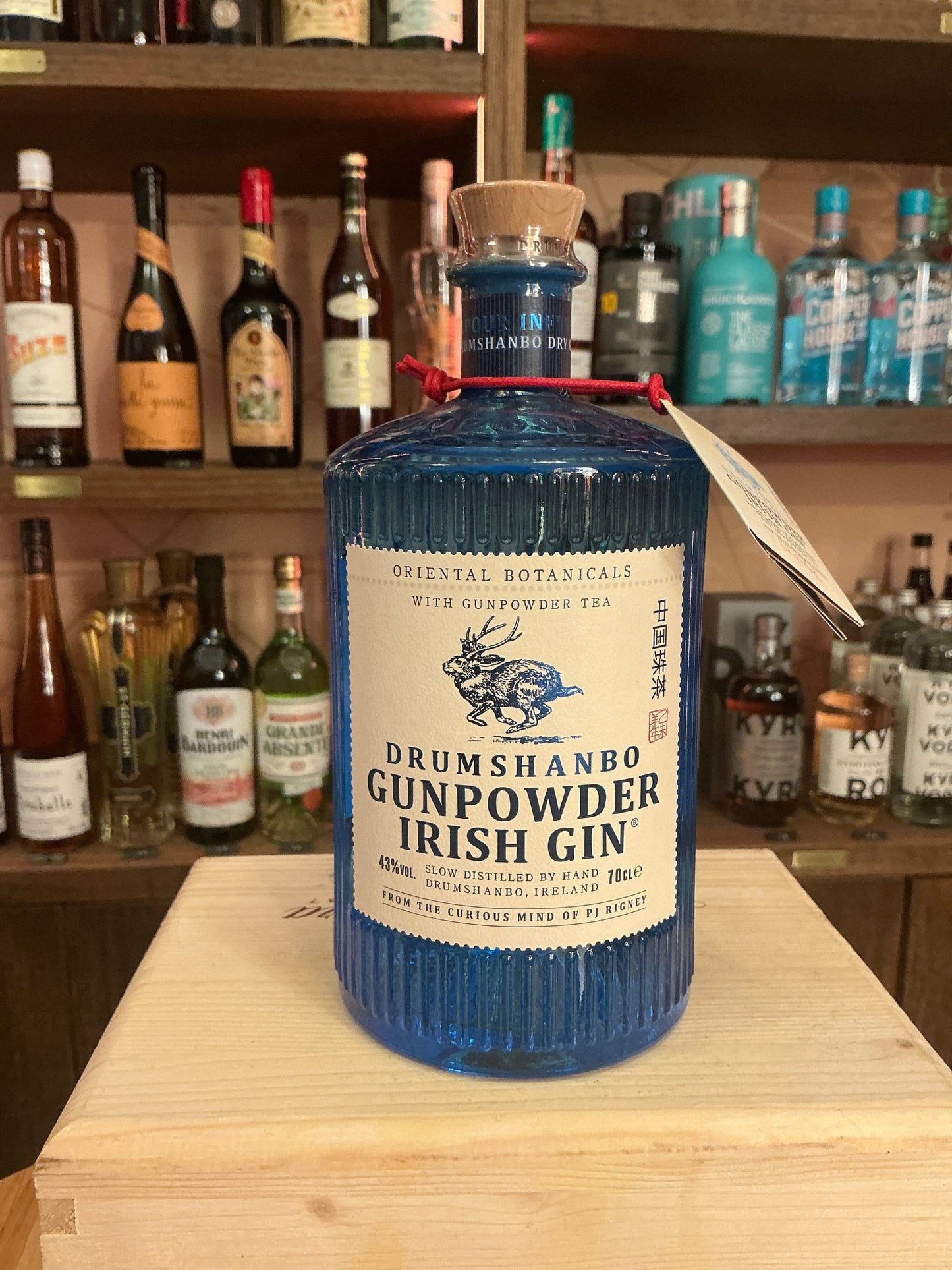 Drumshanbo Gunpowder Irish Gin in a textured blue bottle with wooden stopper and botanical label on wooden surface, premium.
