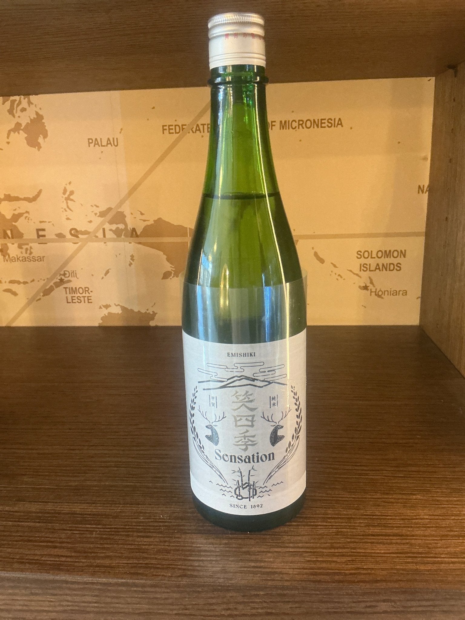 Green glass bottle of Emishiki Sensation White Junmai Ginjo Sake with white label featuring intricate blue design, artisanal .