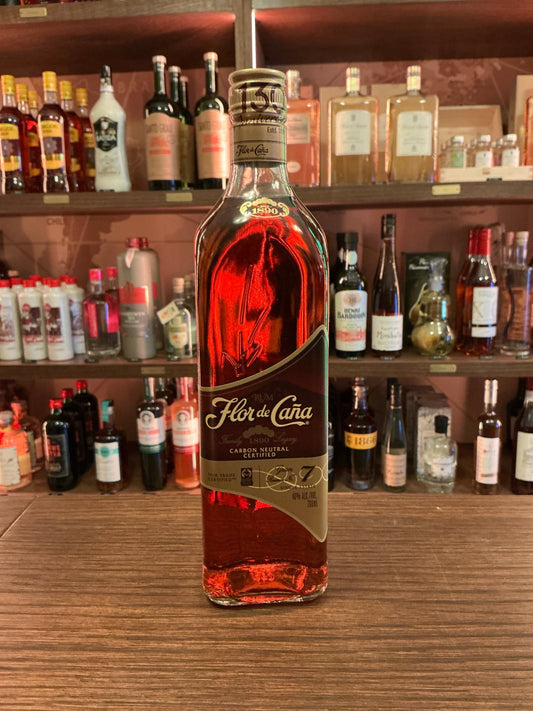 Flor de Caña 7 Year Aged Rum in premium artisan bottle with rich amber color and gold label on rustic wooden bar shelf.
