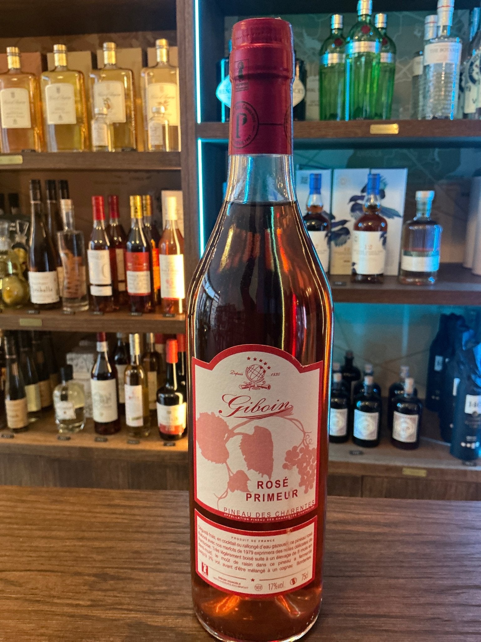 Giboin Pineau Rose Primeur rose wine bottle with red cap, artisan premium fruit spirit on wooden bar counter, specialty.