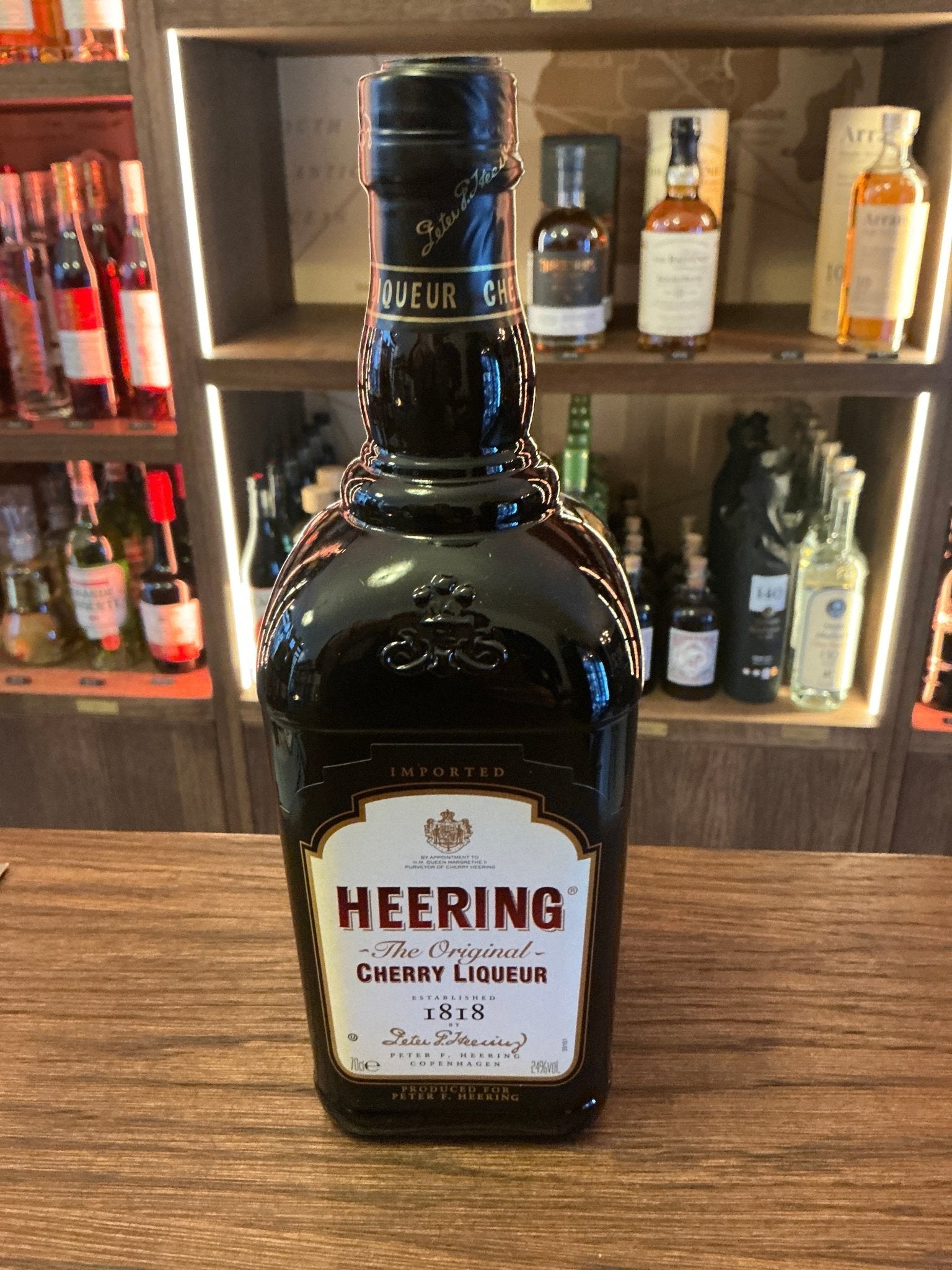 Heering Cherry liqueur bottle with dark glass, premium artisan Dutch spirit, rich cherry flavor, displayed on wooden surface .