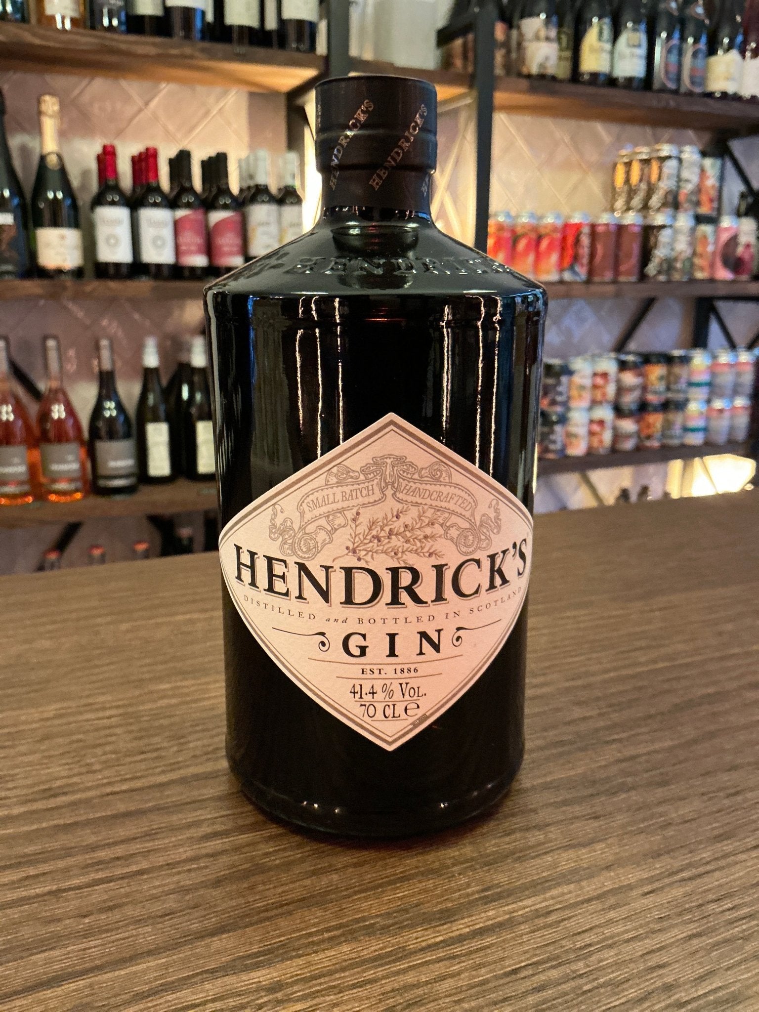 Hendrick’s Gin black bottle with pink diamond label featuring artisan distilled botanical gin on wooden surface in bar.