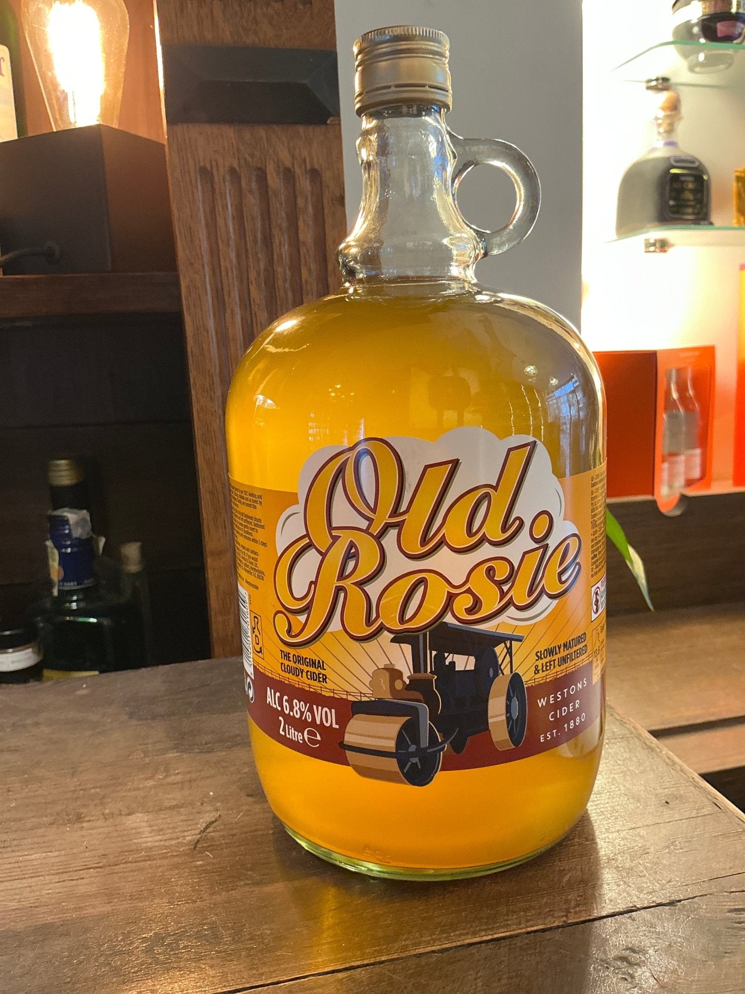 Old Rosie traditional cider in large clear glass bottle with handle, golden amber color, artisan small batch specialty.