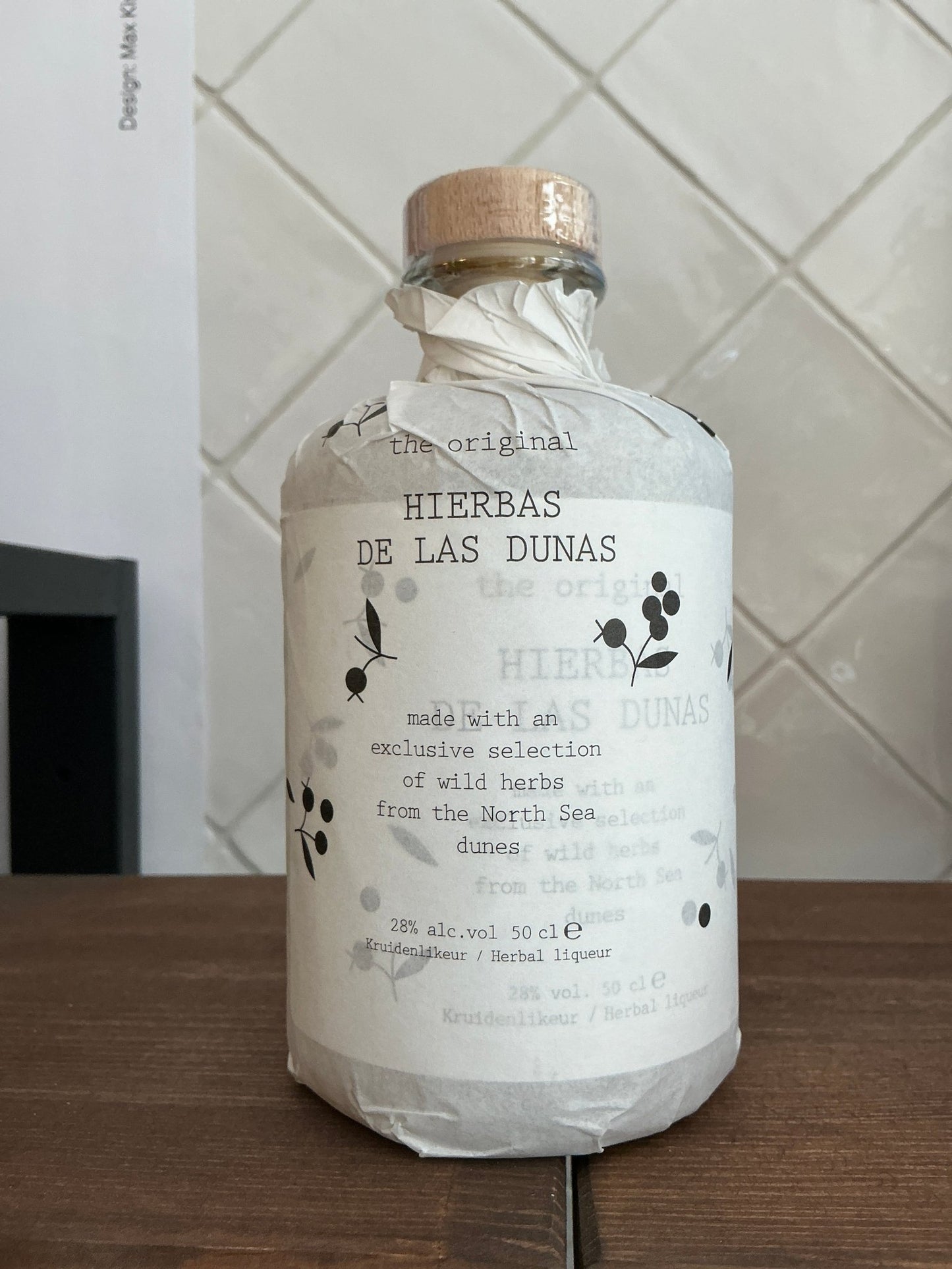 Herbas De Las Dunas premium herbal liqueur bottle wrapped in white paper with cork top, artisan small batch specialty spirit .